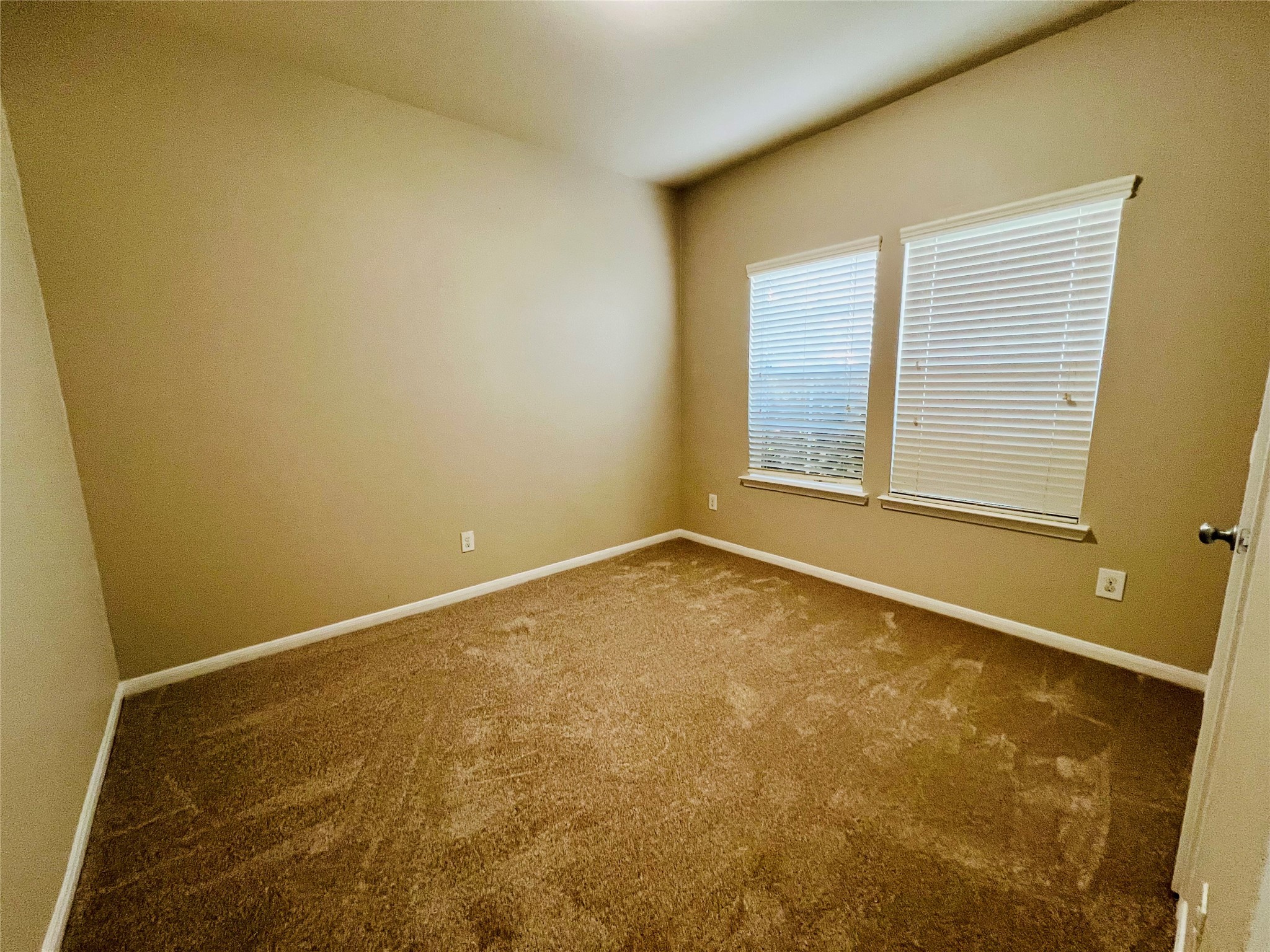 Cozy bedroom with soft carpeting and natural light streaming through dual windows, creating a warm and inviting atmosphere.