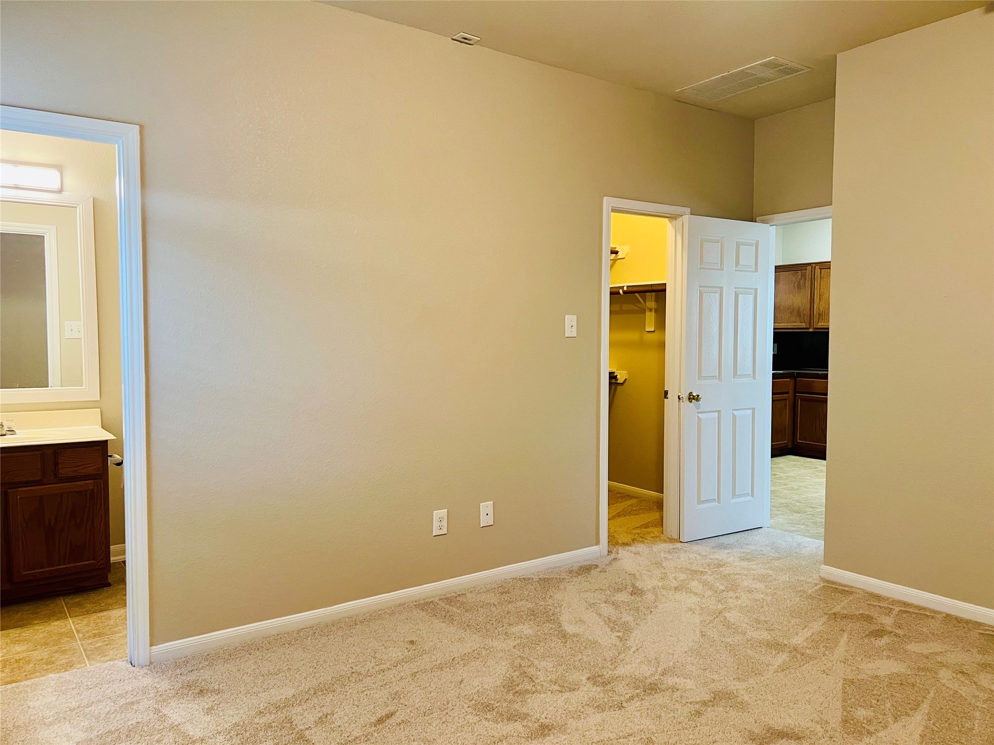 Spacious bedroom with plush carpeting, leading to a walk-in closet and en-suite bathroom, featuring a warm, neutral color palette.