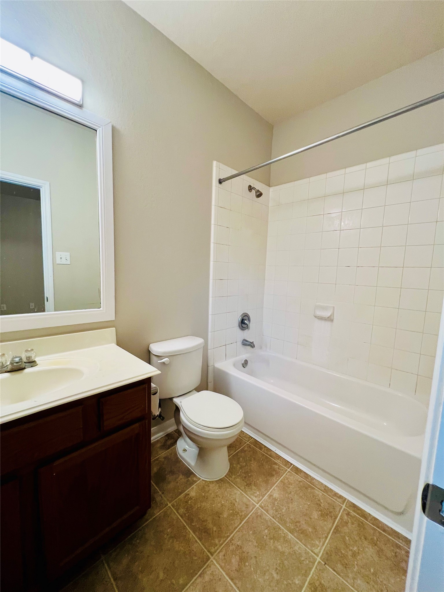 Bright and clean bathroom featuring a tiled shower-tub combination, a sleek vanity with ample storage, and neutral tile flooring.