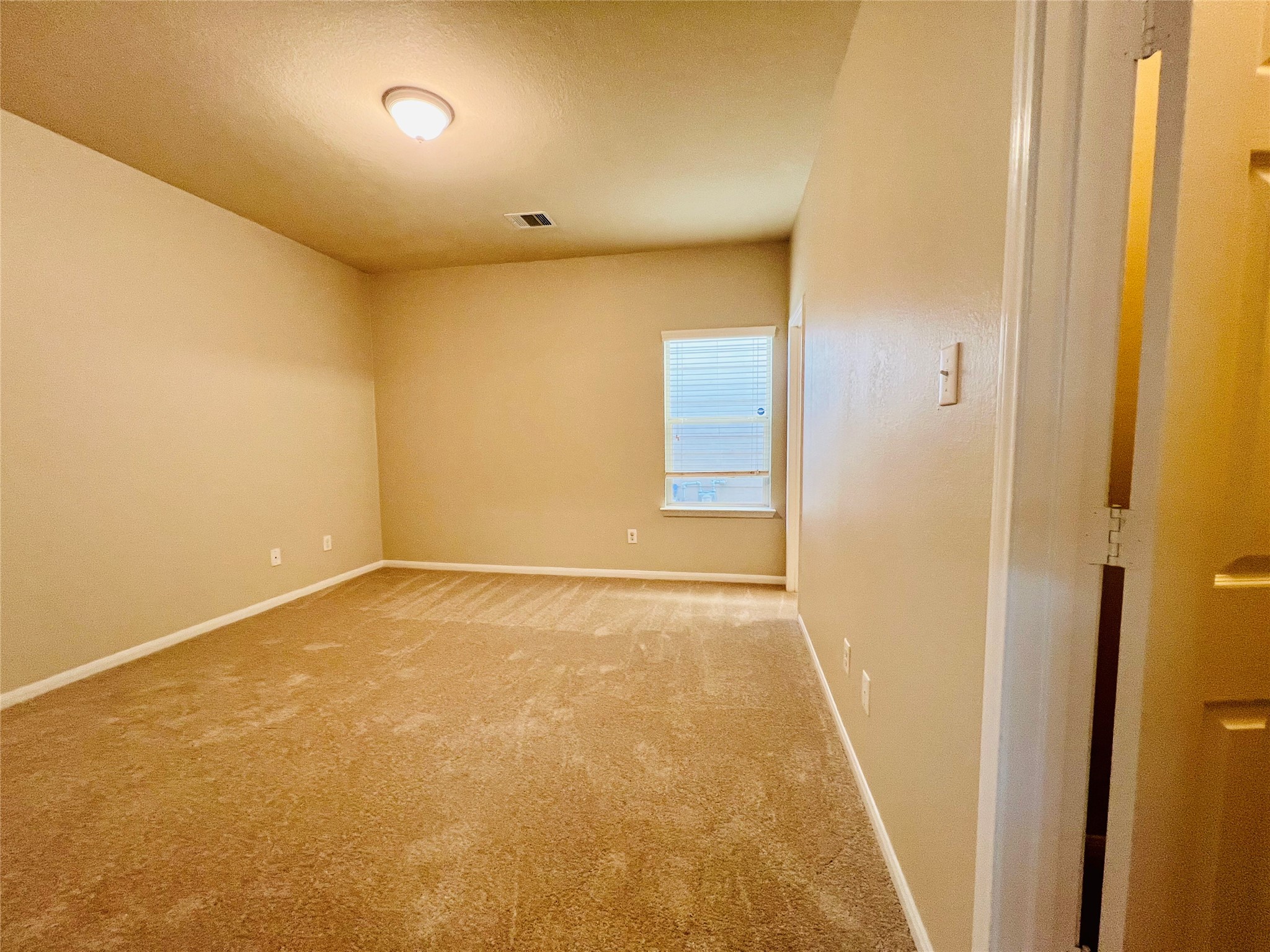 Spacious bedroom with soft carpeting, neutral walls, and ample natural light from a large window.
