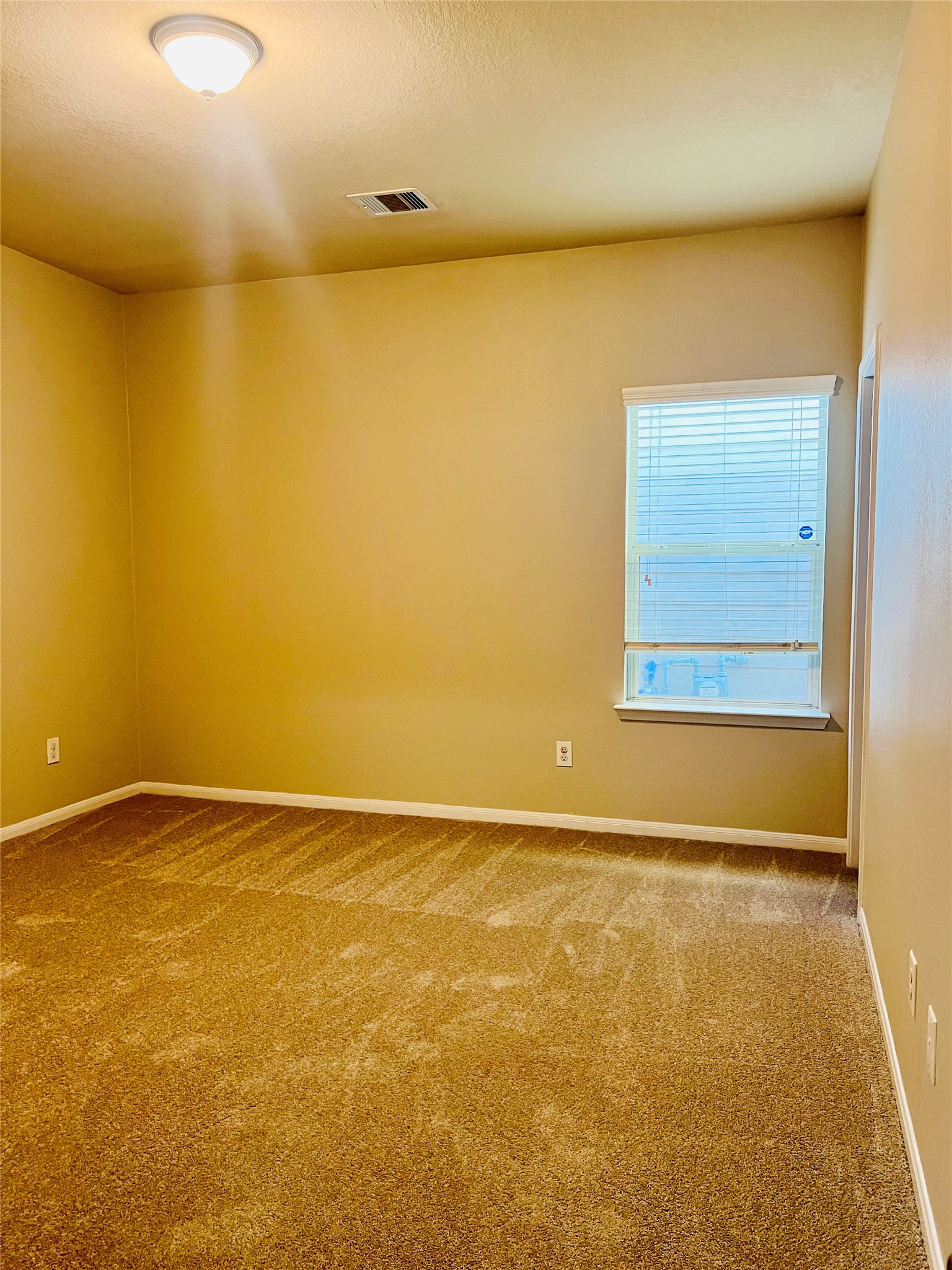 Cozy bedroom featuring warm neutral walls, soft carpeting, and a window that invites natural light.