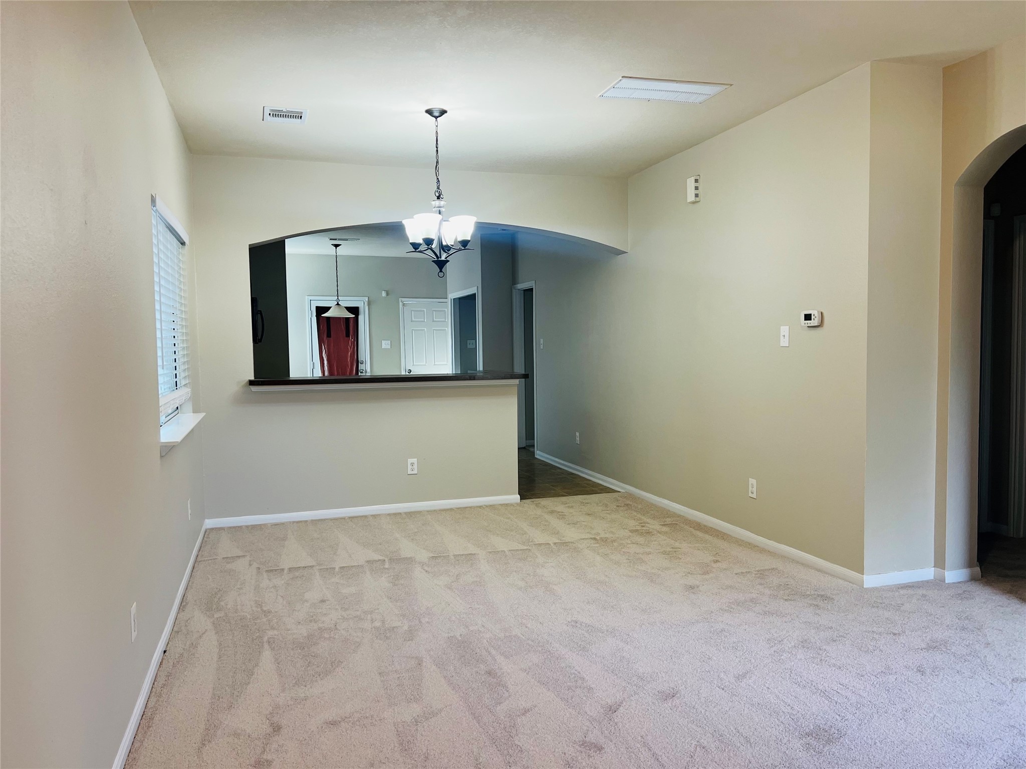 Spacious living area with plush carpet and neutral tones, featuring a modern light fixture and an open archway leading to the kitchen.