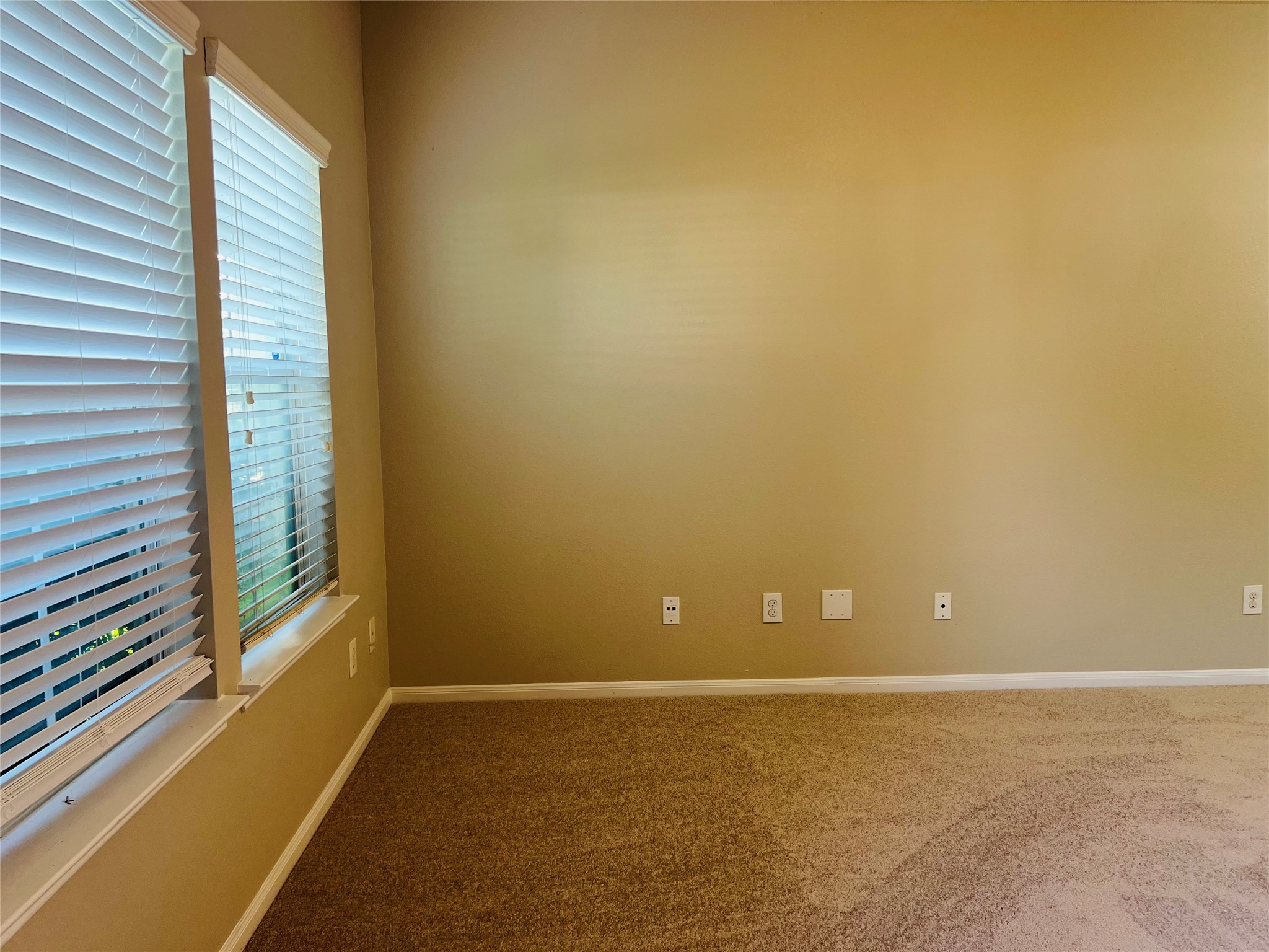 Bright room with neutral walls and soft carpeting, featuring large windows adorned with blinds for ample natural light. Perfect for a cozy retreat or versatile workspace.