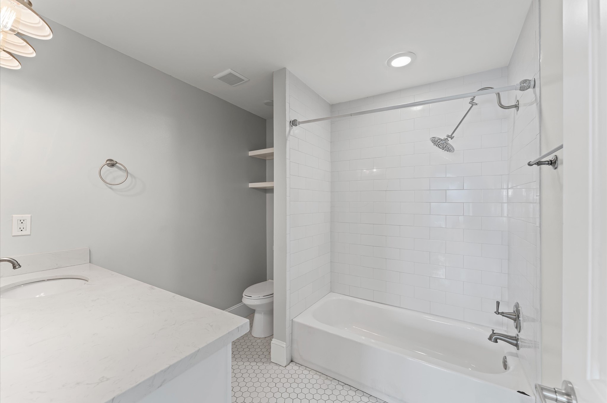 This modern bathroom features a sleek design with a white subway-tiled shower, hexagonal floor tiles, and a spacious vanity. Ample lighting and built-in shelves add functionality and style.