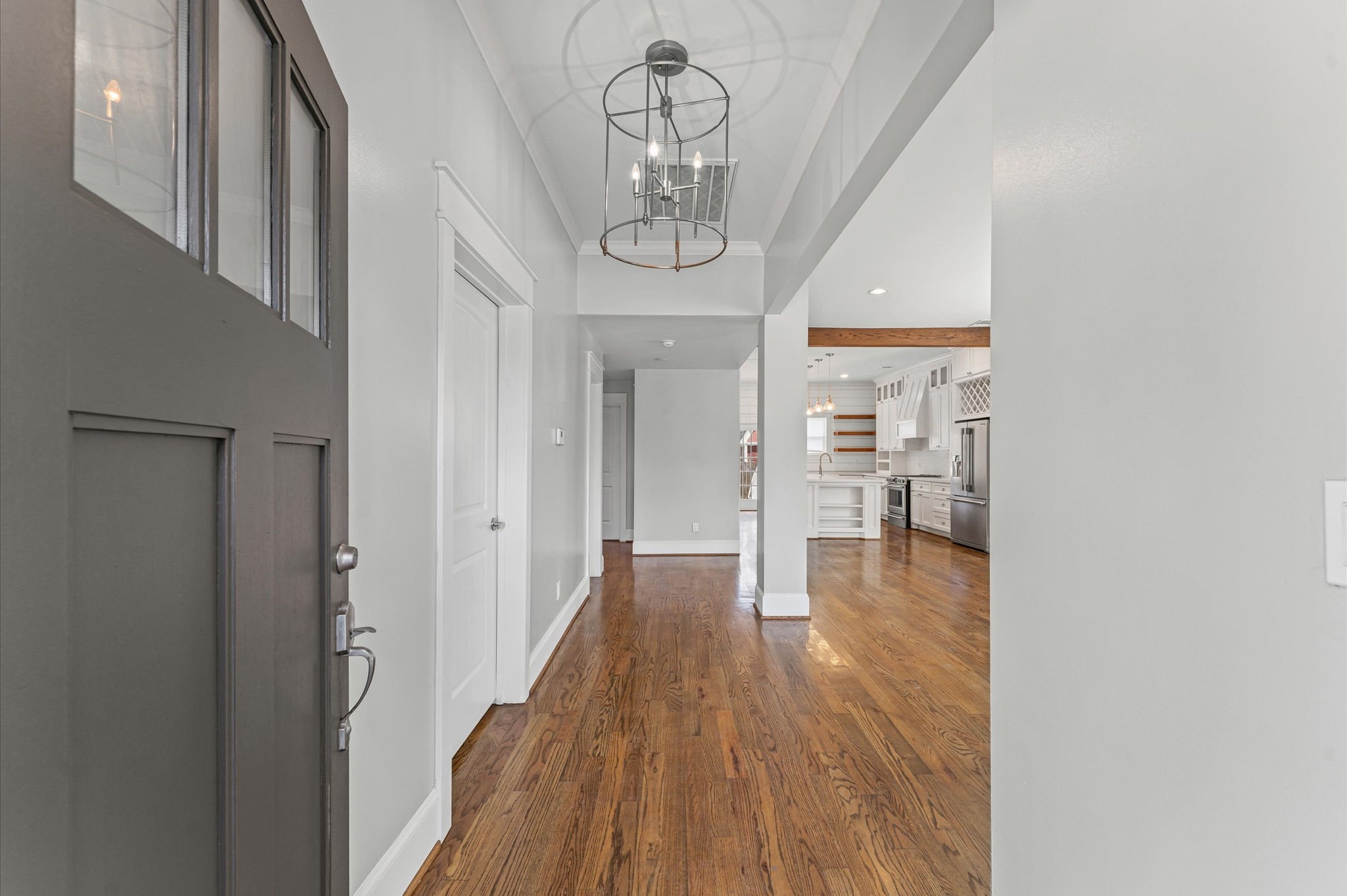 This photo showcases a bright entryway with hardwood floors, leading into an open-concept kitchen. The space features modern lighting, white cabinetry, and stainless steel appliances, creating a welcoming and contemporary feel.
