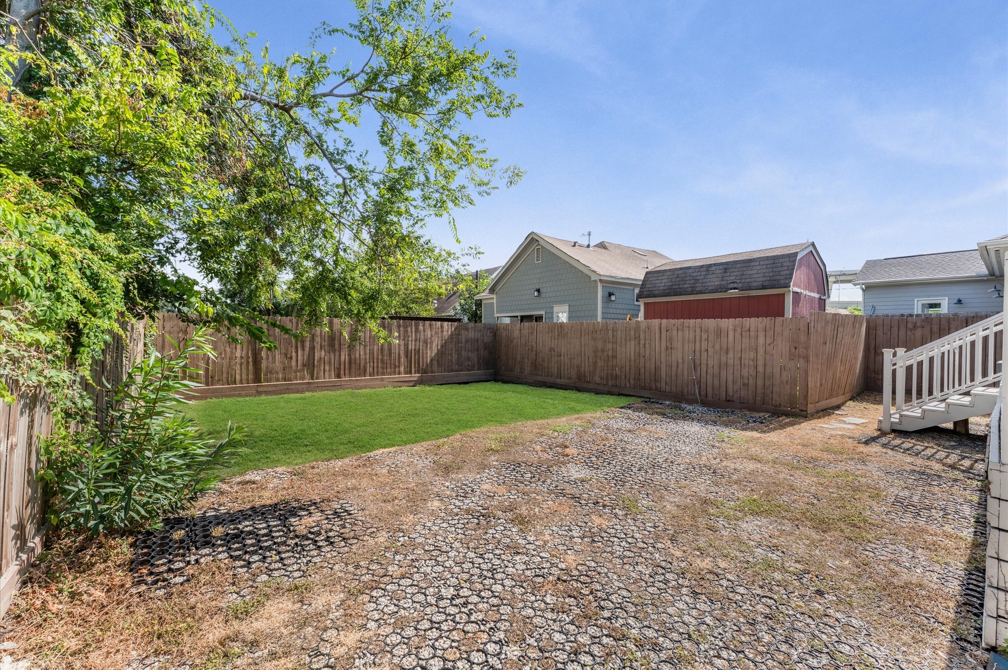 This backyard features a mix of green lawn and gravel area, enclosed by a wooden fence. It offers a spacious outdoor area with a small tree for shade and a storage shed in the back. Perfect for gardening or entertaining.