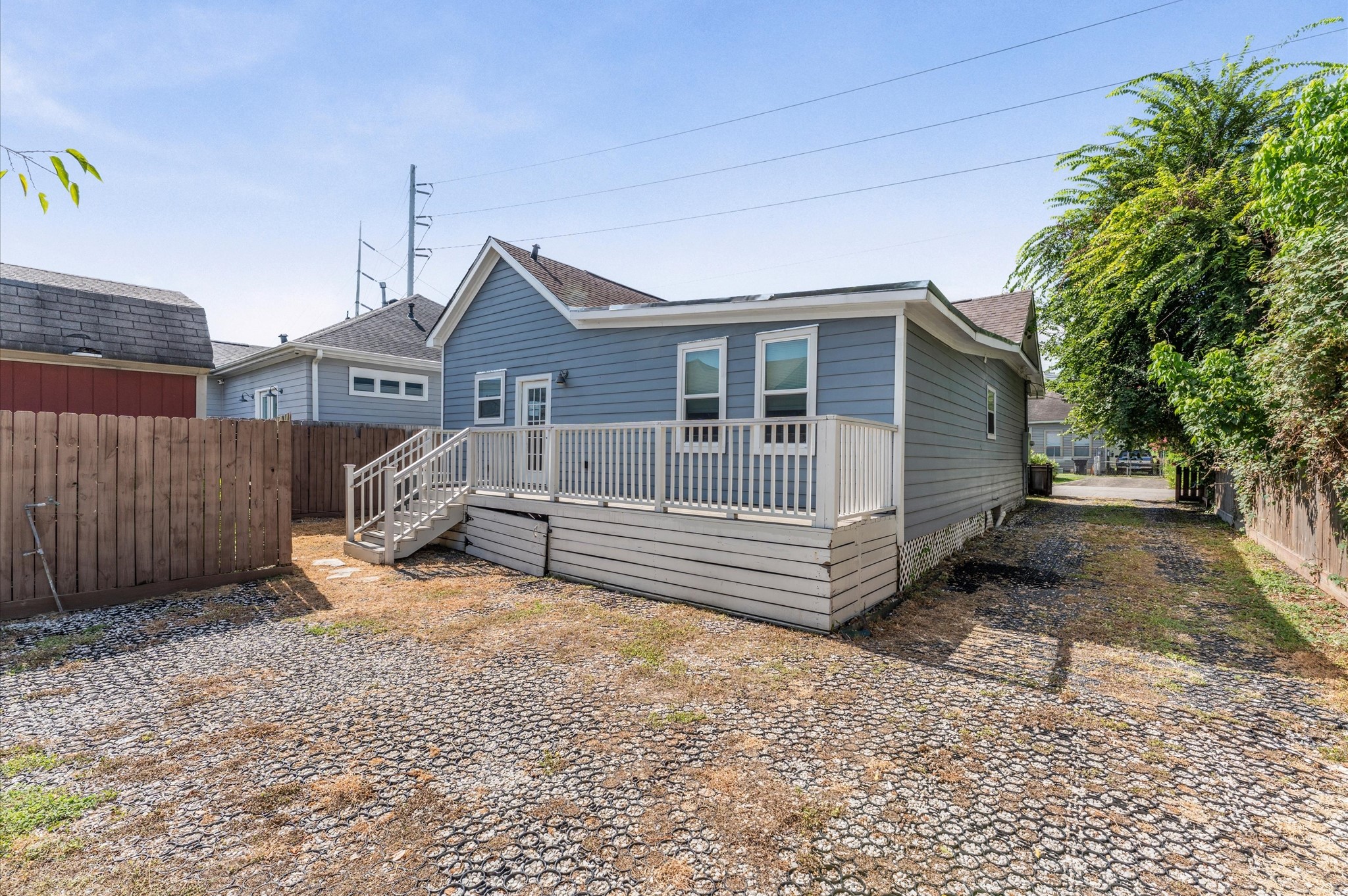 This photo showcases the back exterior of a charming blue house with a small deck and steps leading to a fenced yard. The yard features a gravel and grass area, ideal for low maintenance.