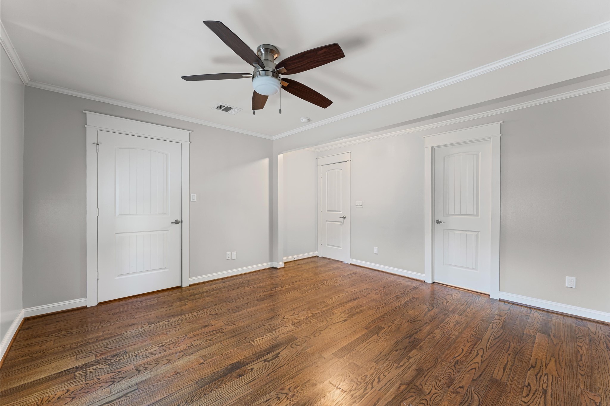 This room features polished hardwood floors, neutral gray walls, white trim, and a ceiling fan, with multiple doors for easy access and storage.
