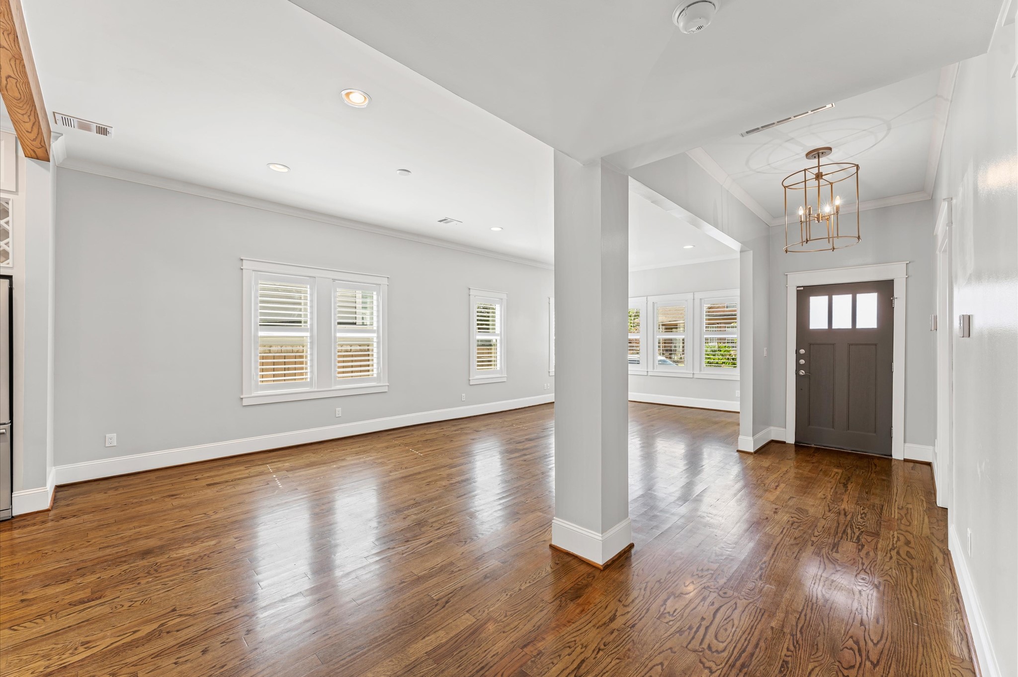 Bright and spacious open-concept living area with hardwood floors, large windows, and a modern light fixture. Features a welcoming entryway with a stylish front door.