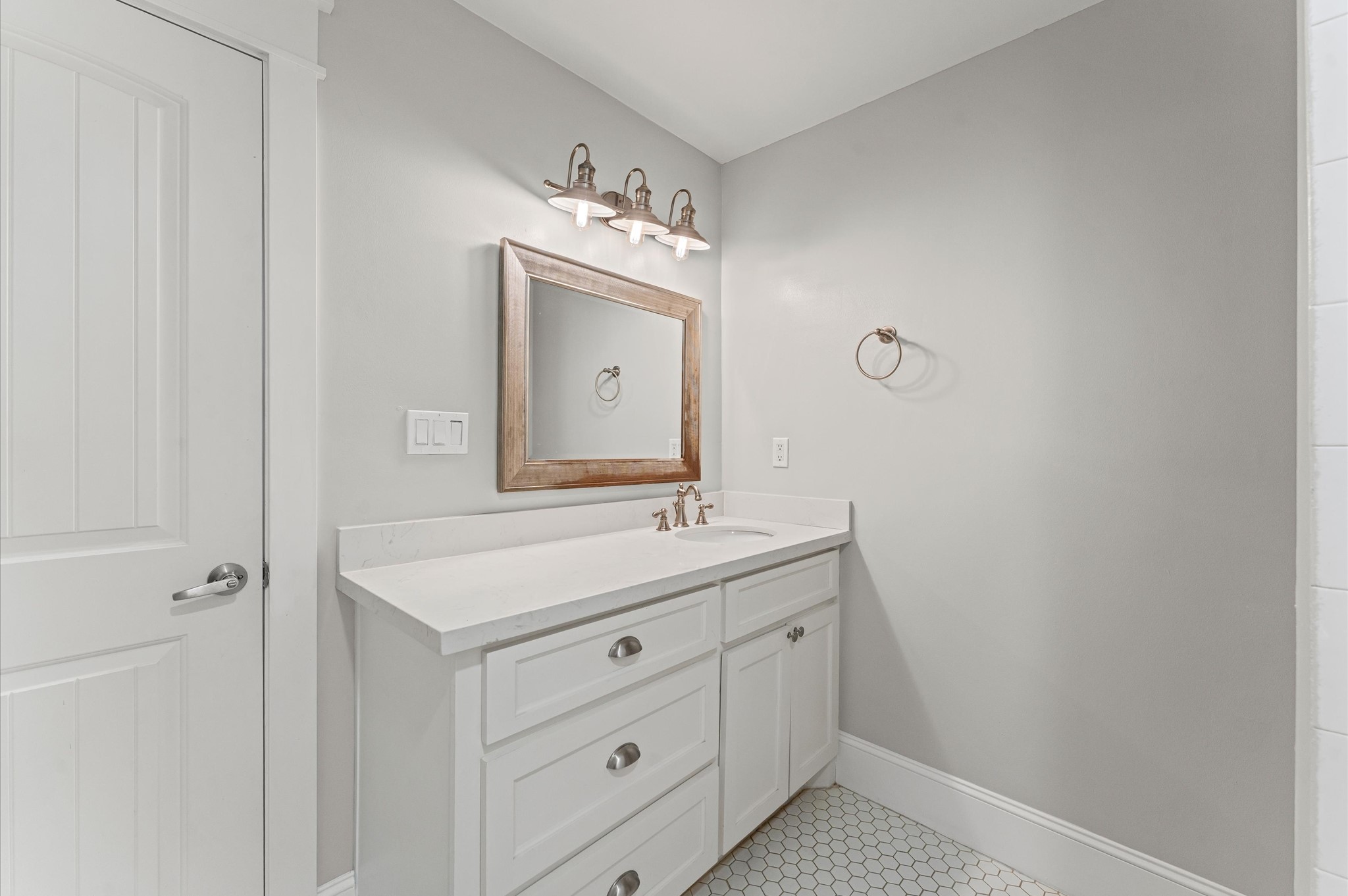 This bathroom features a modern design with a light gray color scheme, a white vanity with ample storage, and a stylish wooden-framed mirror. The space is well-lit with elegant overhead lighting and has a sleek, clean look.