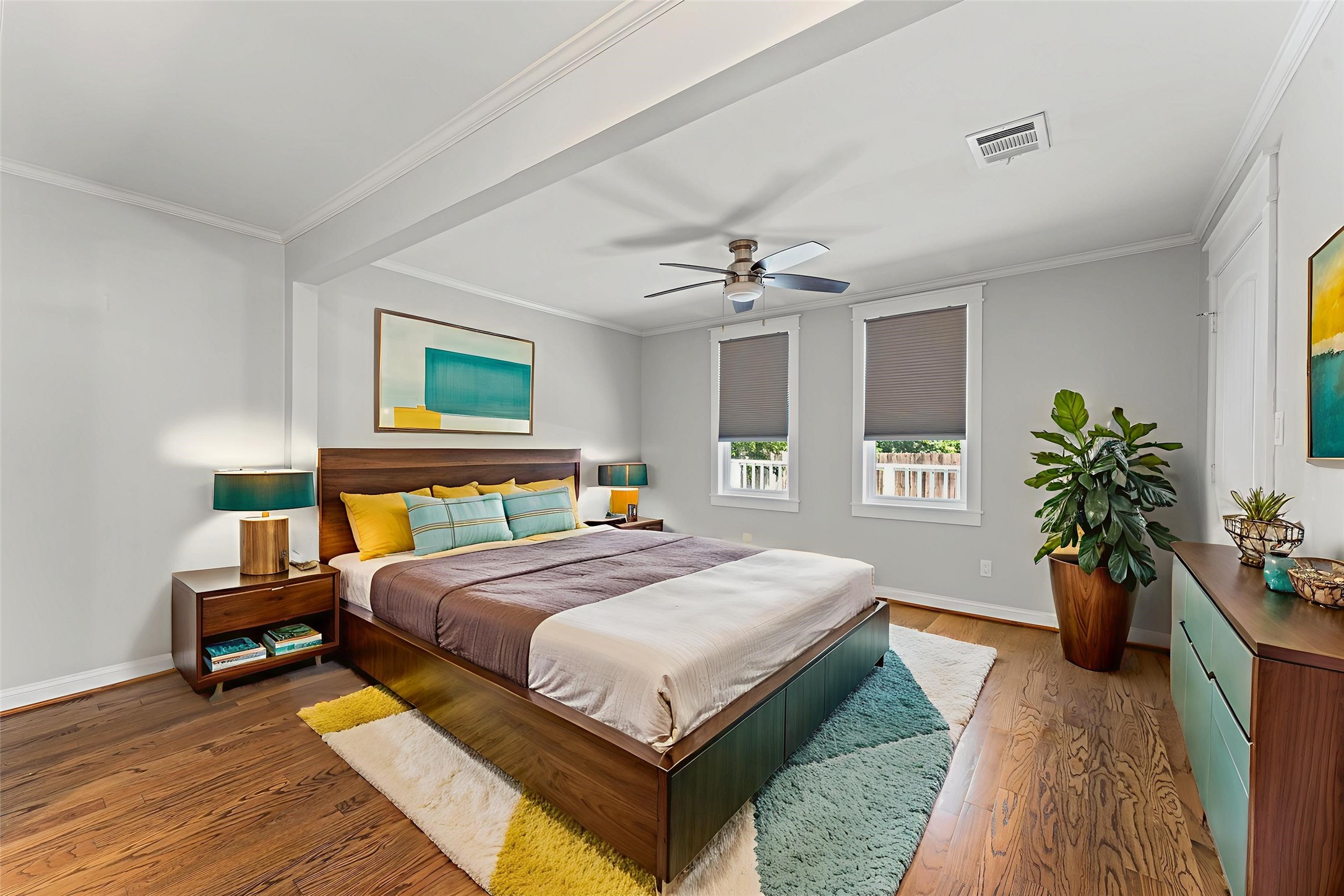 This bedroom features a modern design with hardwood floors. It has a ceiling fan, two windows with shades add to the cozy atmosphere.