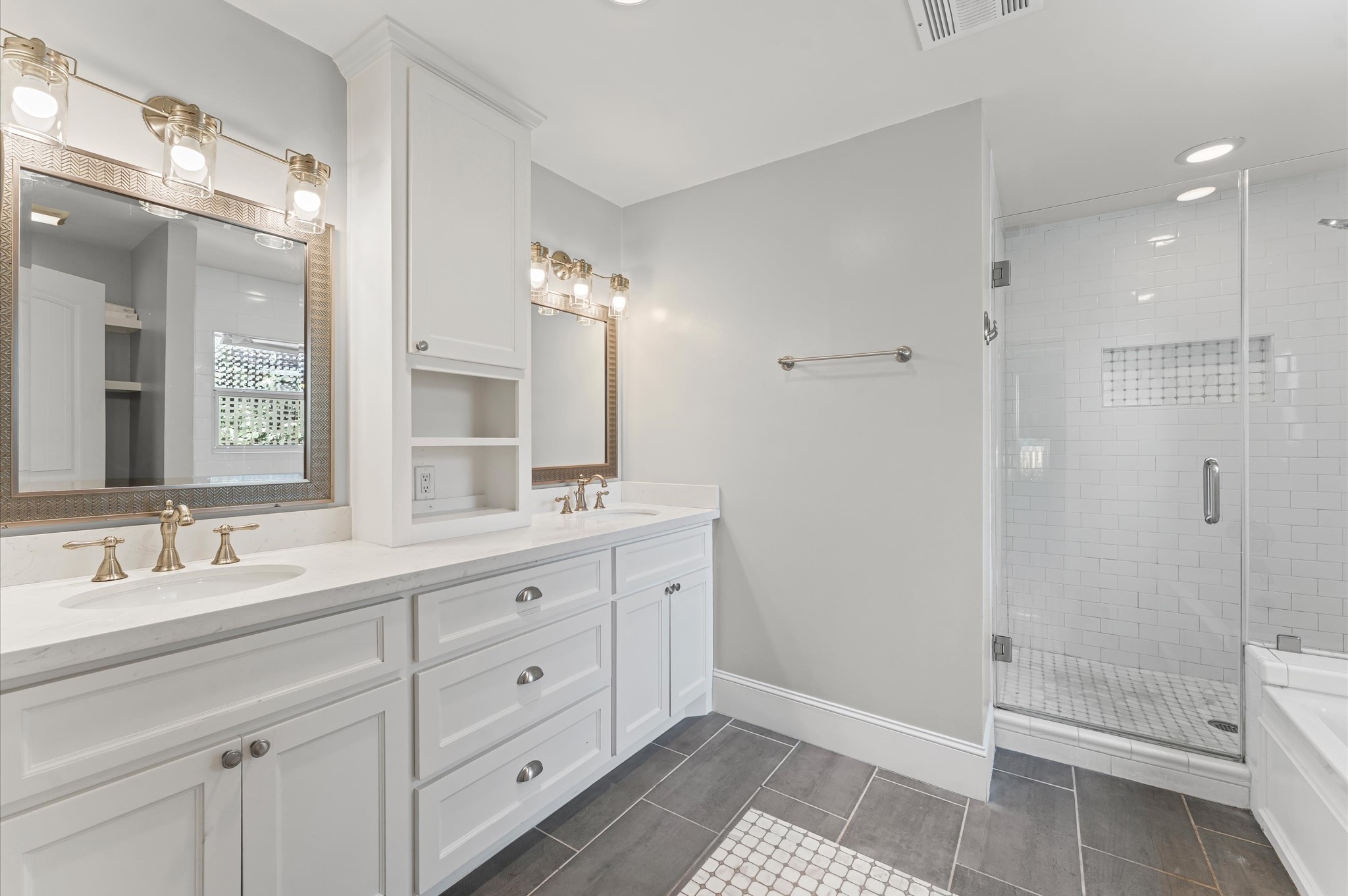 This bright and modern bathroom features dual sinks with elegant fixtures, ample cabinetry, a spacious walk-in shower with subway tile, and stylish lighting.