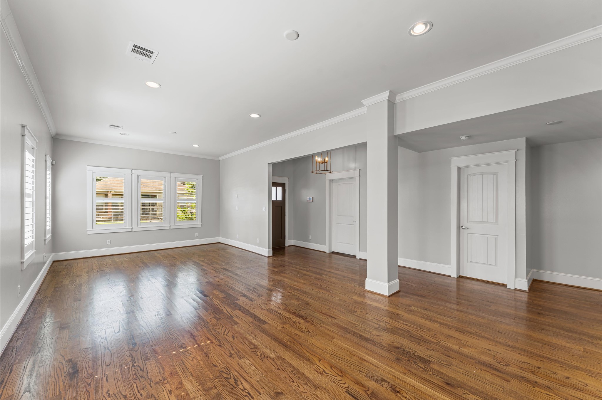 Spacious, bright living area with hardwood floors, neutral walls, and recessed lighting. Features large windows, elegant trim, and a modern light fixture near the entrance. Ideal for versatile living arrangements.