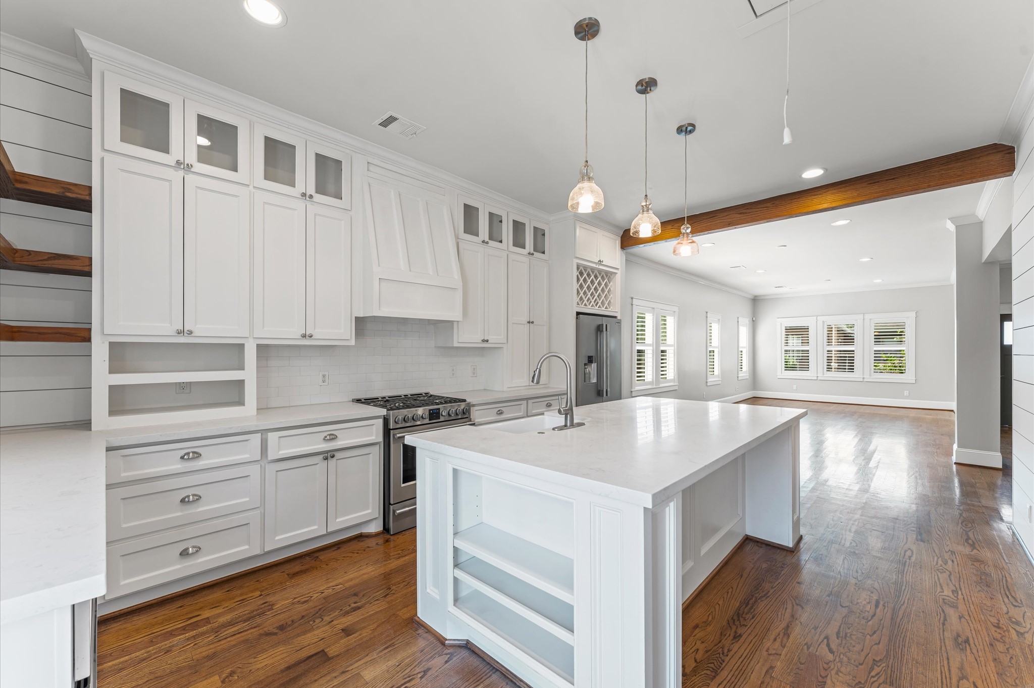 This spacious, modern kitchen features sleek white cabinetry, a large island with a sink, and stainless steel appliances. Hardwood floors and ample natural light create a warm, inviting atmosphere. Ideal for entertaining and family gatherings.