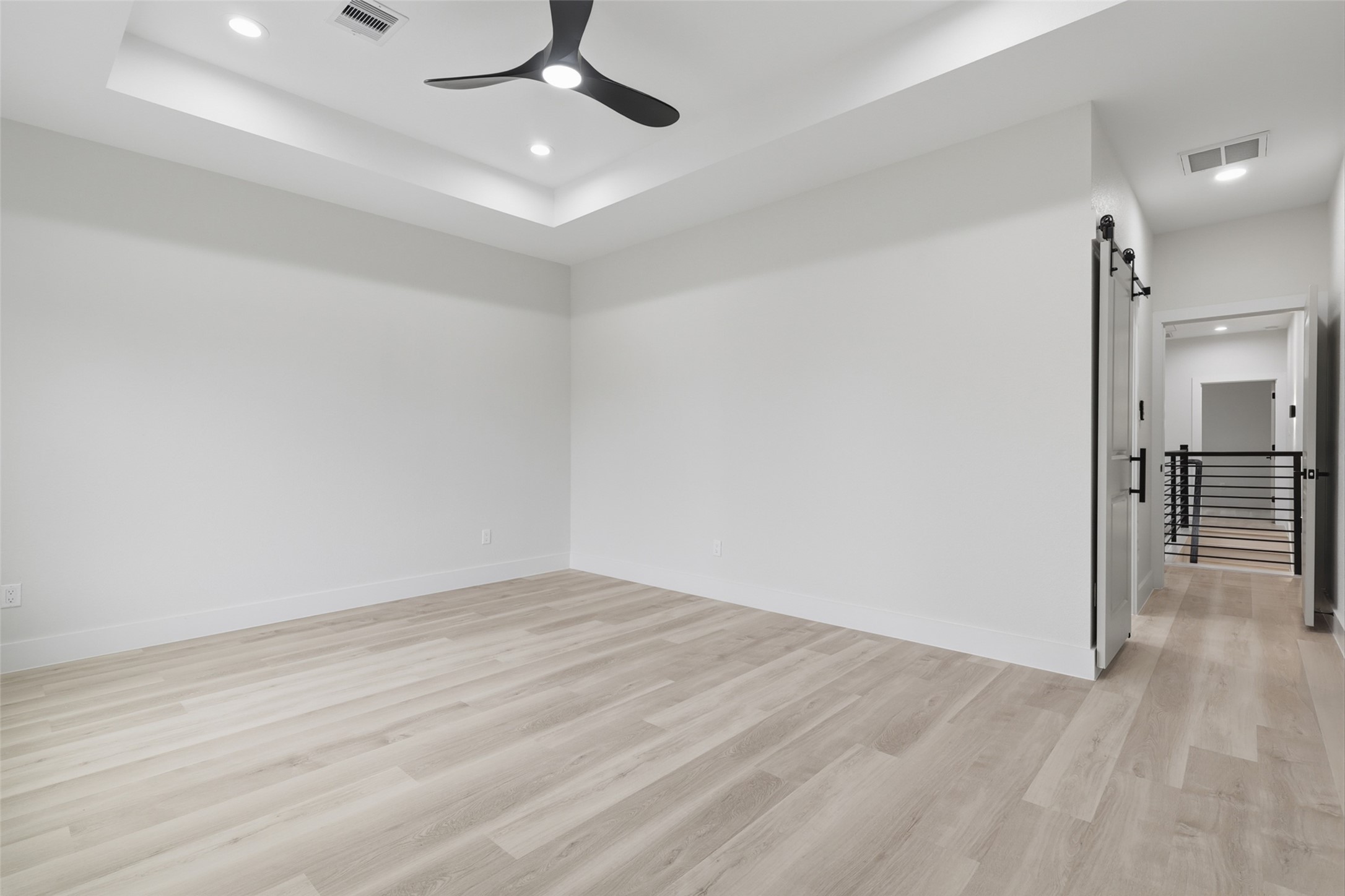 Spacious primary bedroom with sleek light wood LVP flooring, modern recessed lighting, and a stylish ceiling fan, offering a contemporary and airy atmosphere.