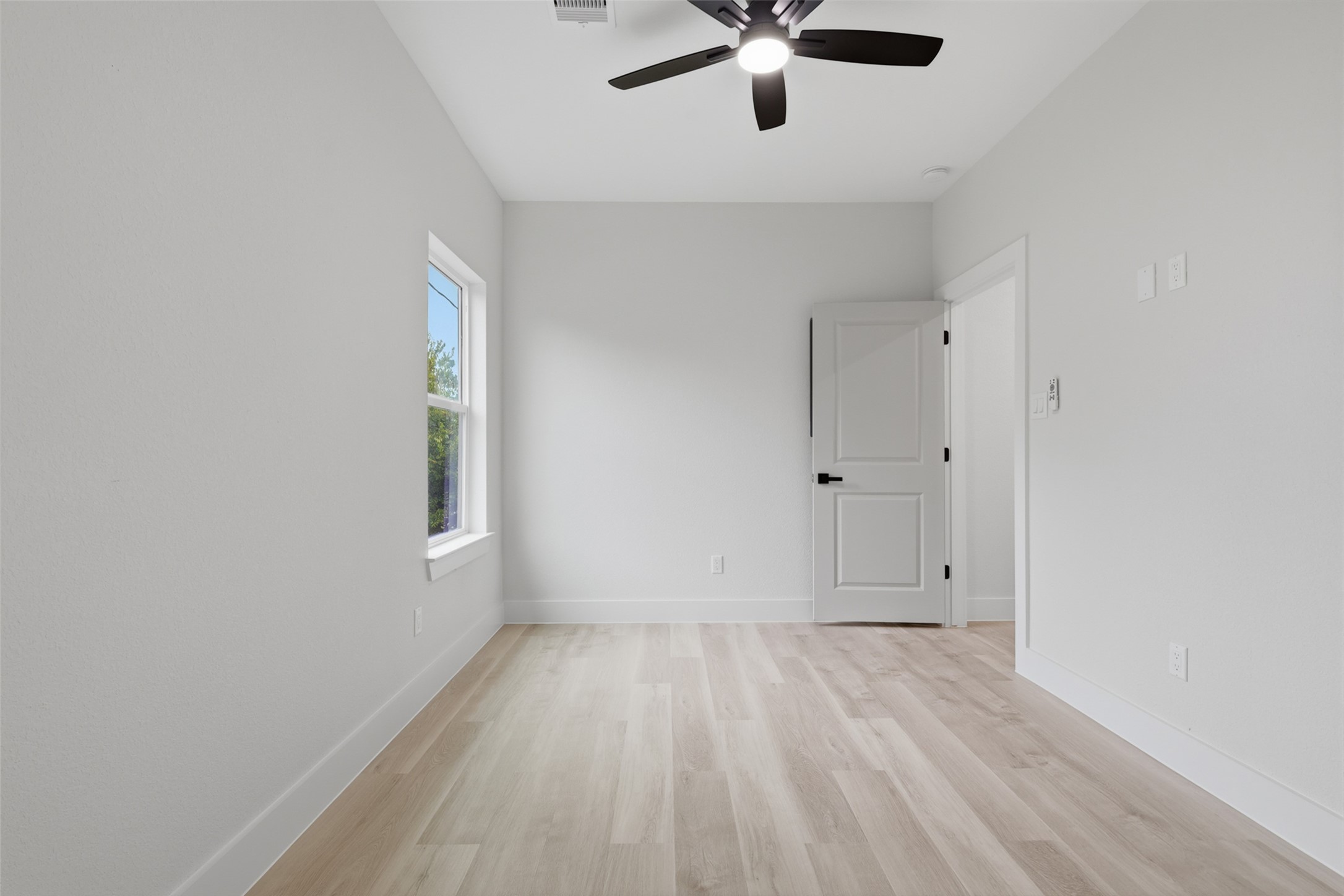 Bright and airy room featuring sleek light wood like LVP flooring, a modern ceiling fan, and ample natural light from the window, perfect for a cozy bedroom and an office space for a student or child.
