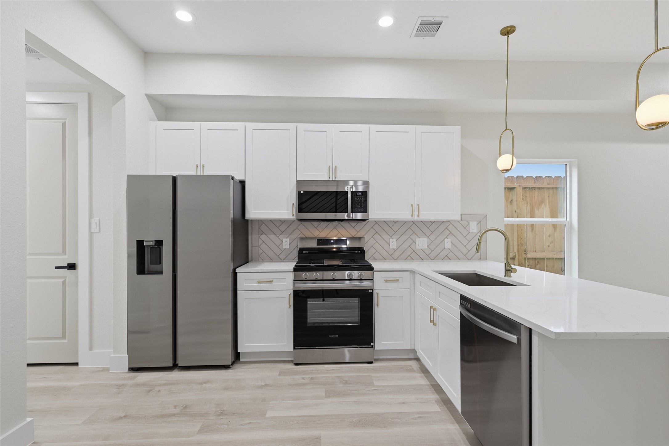 Sleek modern kitchen featuring stainless steel appliances, crisp white cabinetry, and a stylish herringbone backsplash, complemented by elegant pendant lighting.