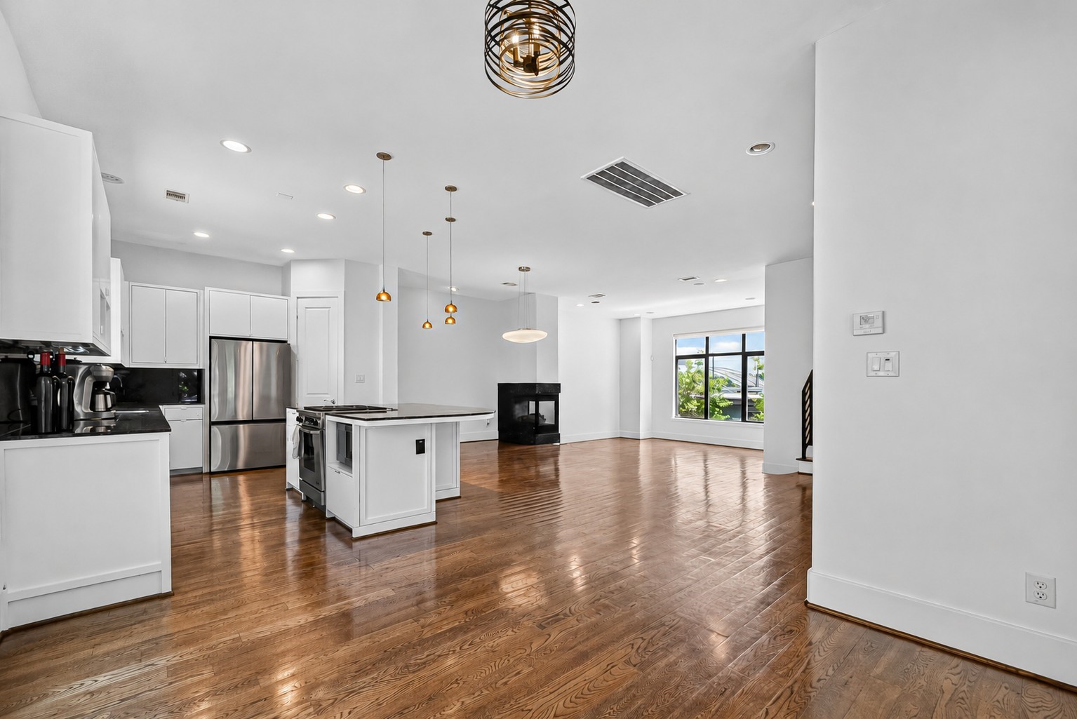 Spacious open-concept living area with gleaming hardwood floors, a modern kitchen featuring stainless steel appliances, and a cozy fireplace. Large windows provide abundant natural light and scenic views.