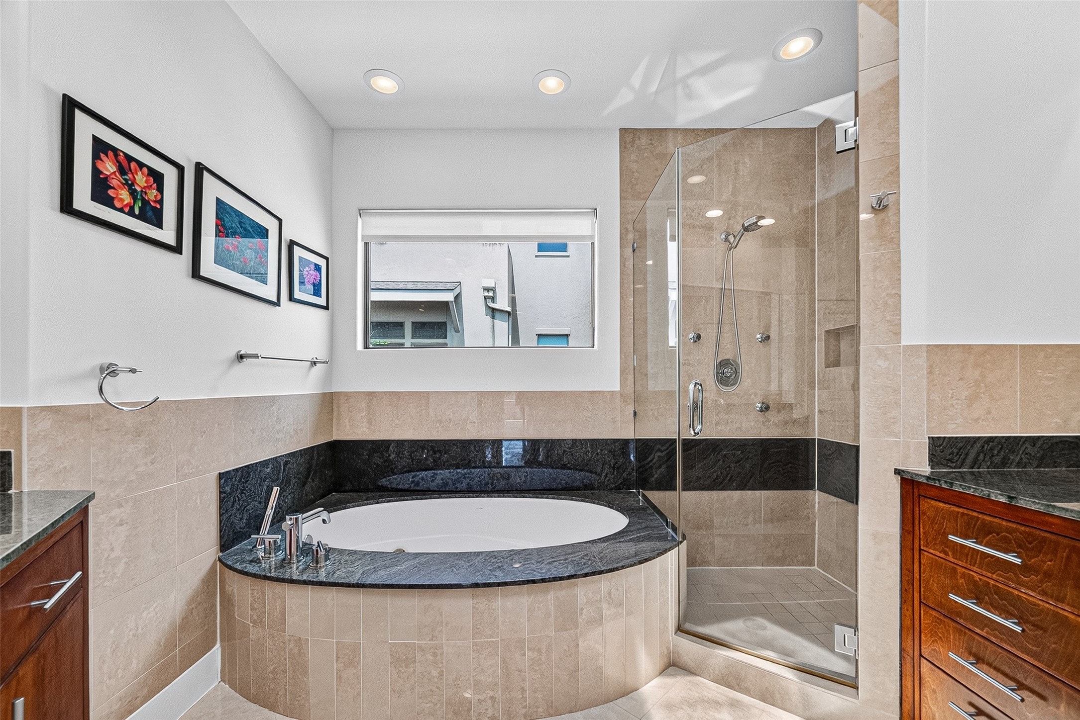 Luxurious primary bathroom featuring a spa-like soaking tub with elegant black trim, a spacious glass-enclosed shower, and stylish wood cabinetry, all complemented by modern recessed lighting and tasteful artwork.