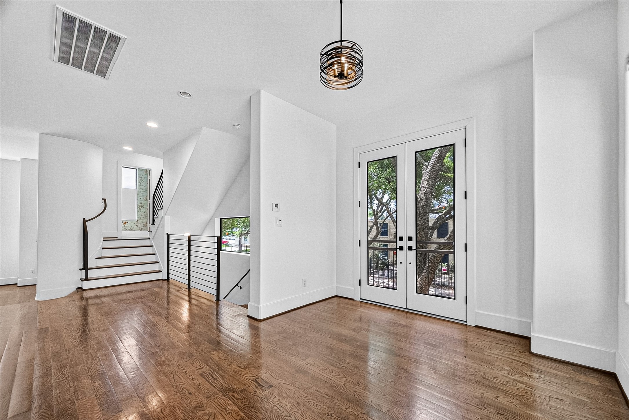 Bright and inviting breakfast area with elegant hardwood floors, modern lighting, and glass double doors leading to a patio. A sleek staircase enhances the contemporary design.