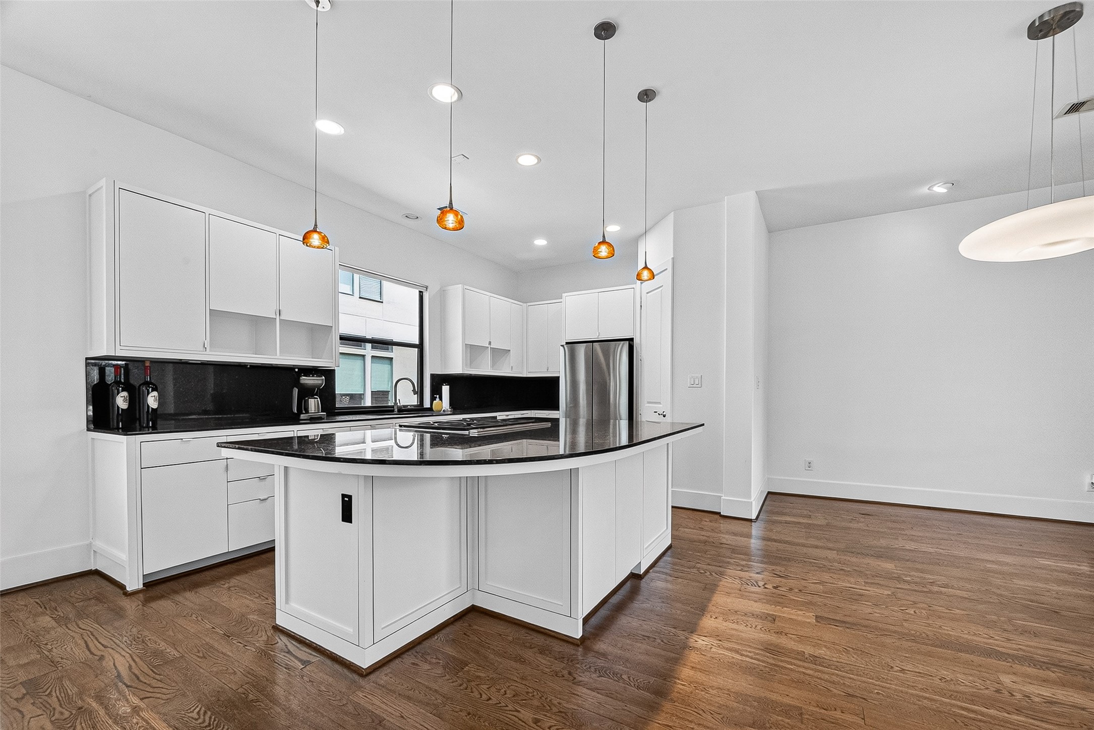 Modern kitchen with sleek white cabinetry, a spacious island with dark countertops, and elegant pendant lighting, all set against warm hardwood floors.