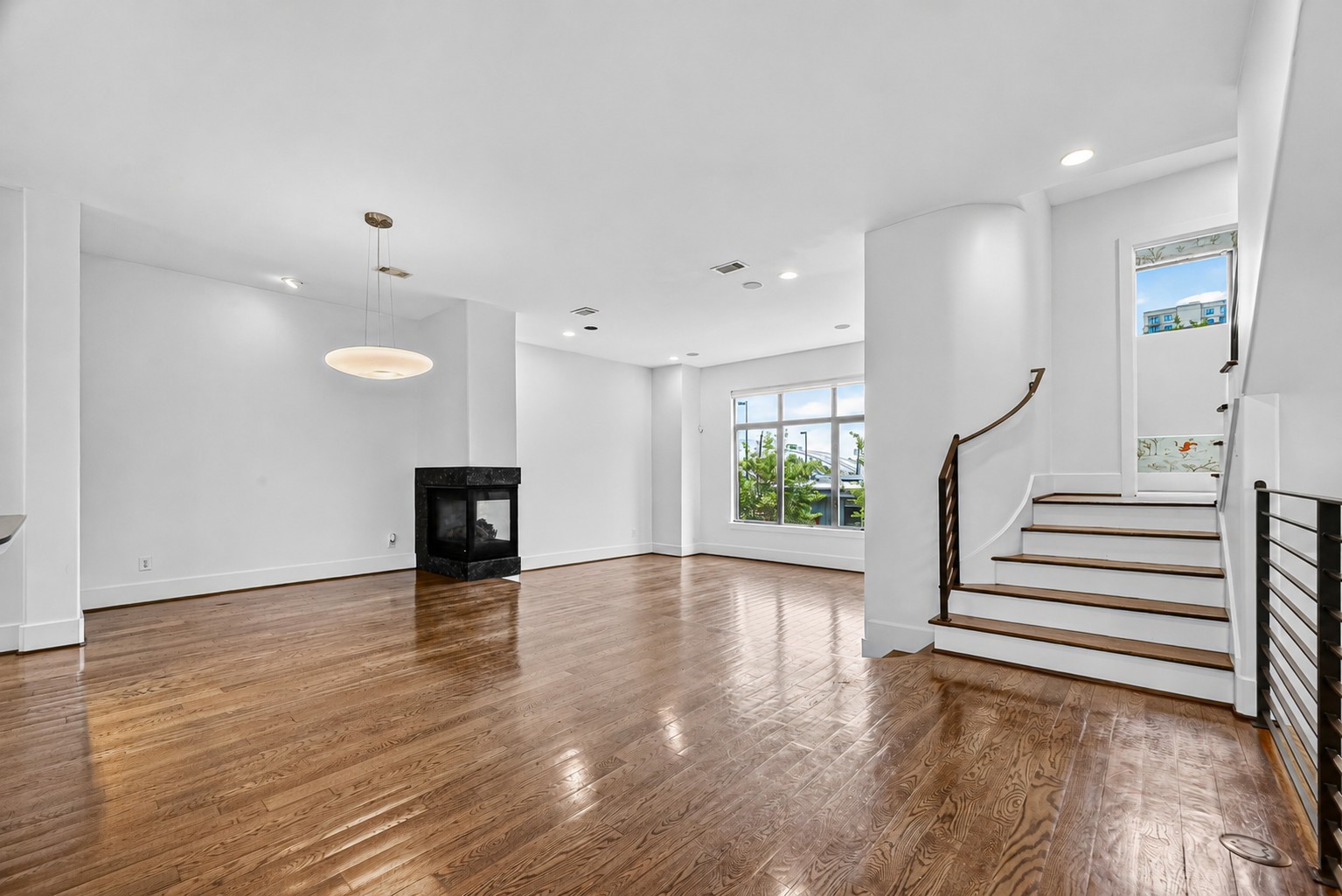 Spacious living area with elegant hardwood floors, a modern fireplace, large windows for natural light, and a stylish curved staircase.