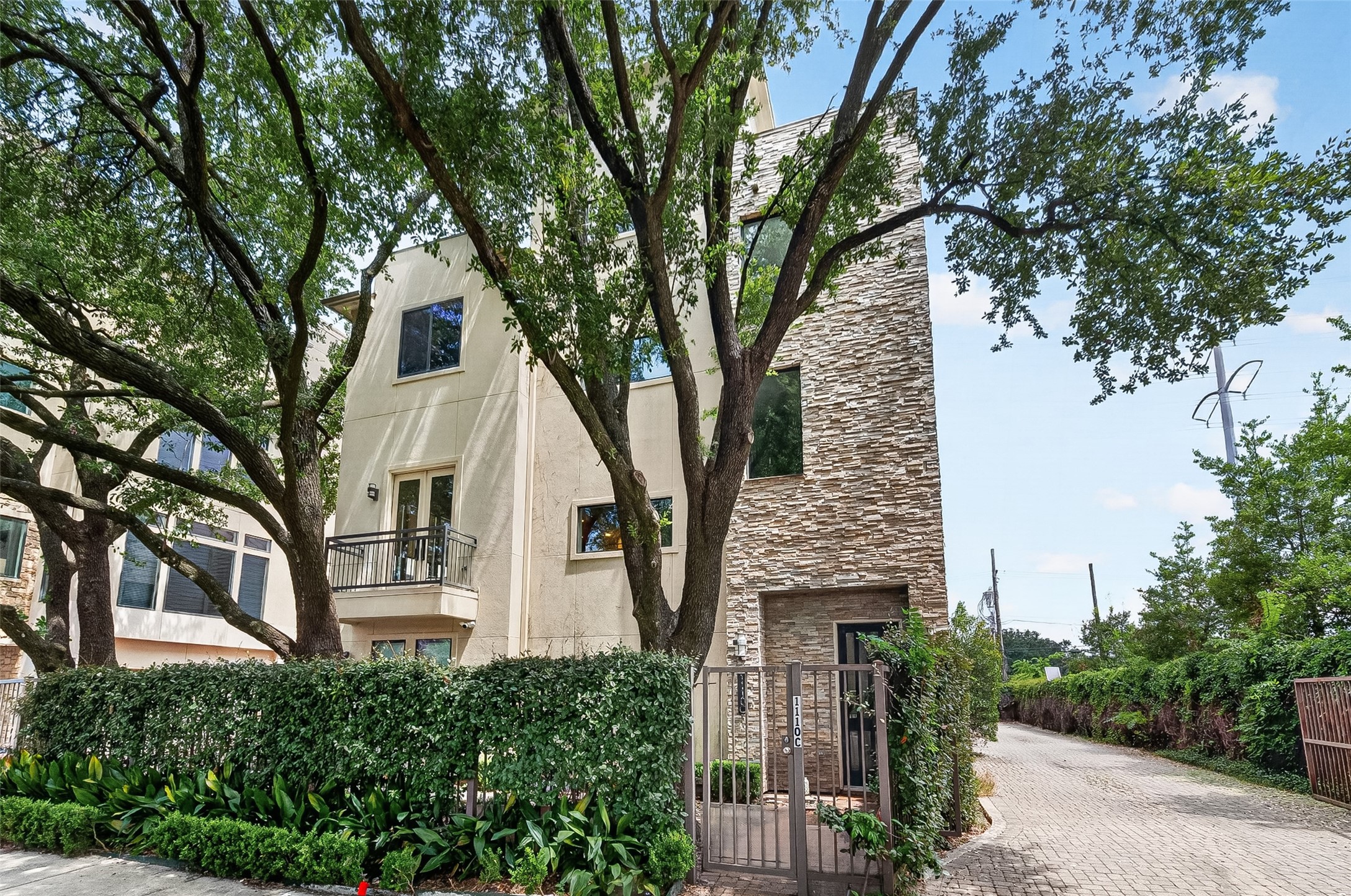 Modern townhome featuring a striking stone facade and private balcony, set amidst lush greenery and mature trees.