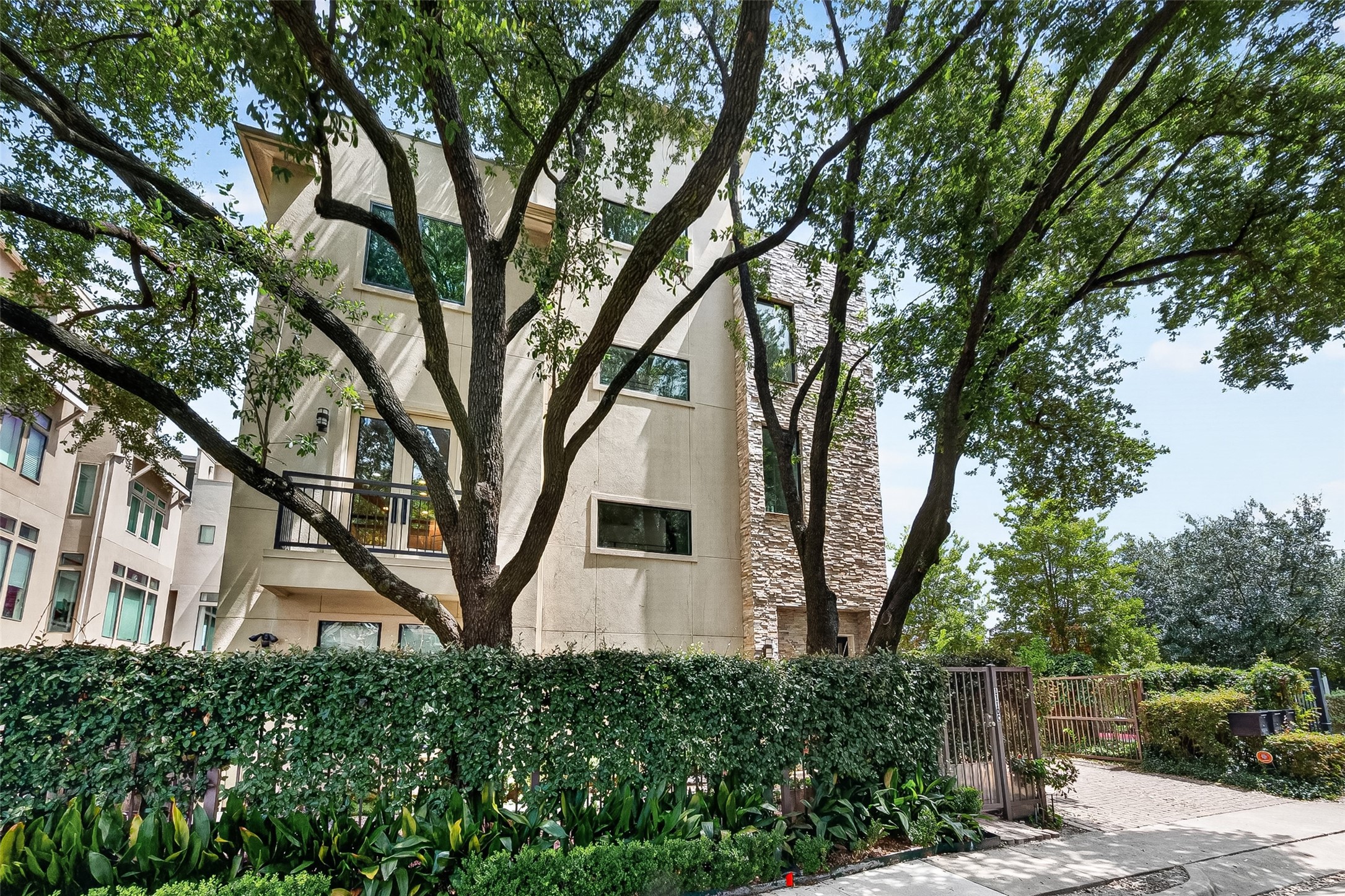Contemporary multi-story home nestled among mature trees, featuring a blend of stone and stucco exterior with lush landscaping for added privacy.