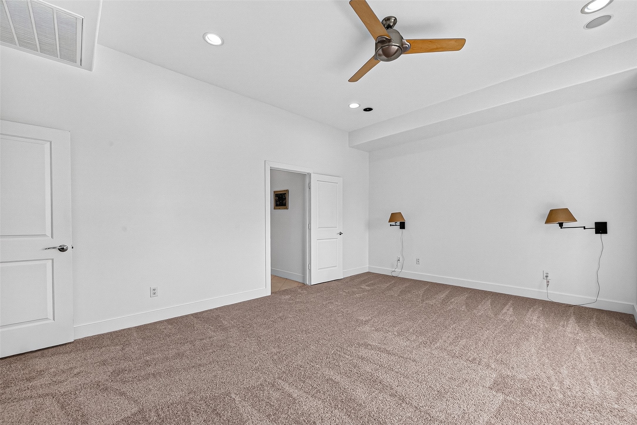 Spacious primary bedroom with plush carpeting, recessed lighting, and a stylish ceiling fan, offering a clean, modern design perfect for relaxation.
