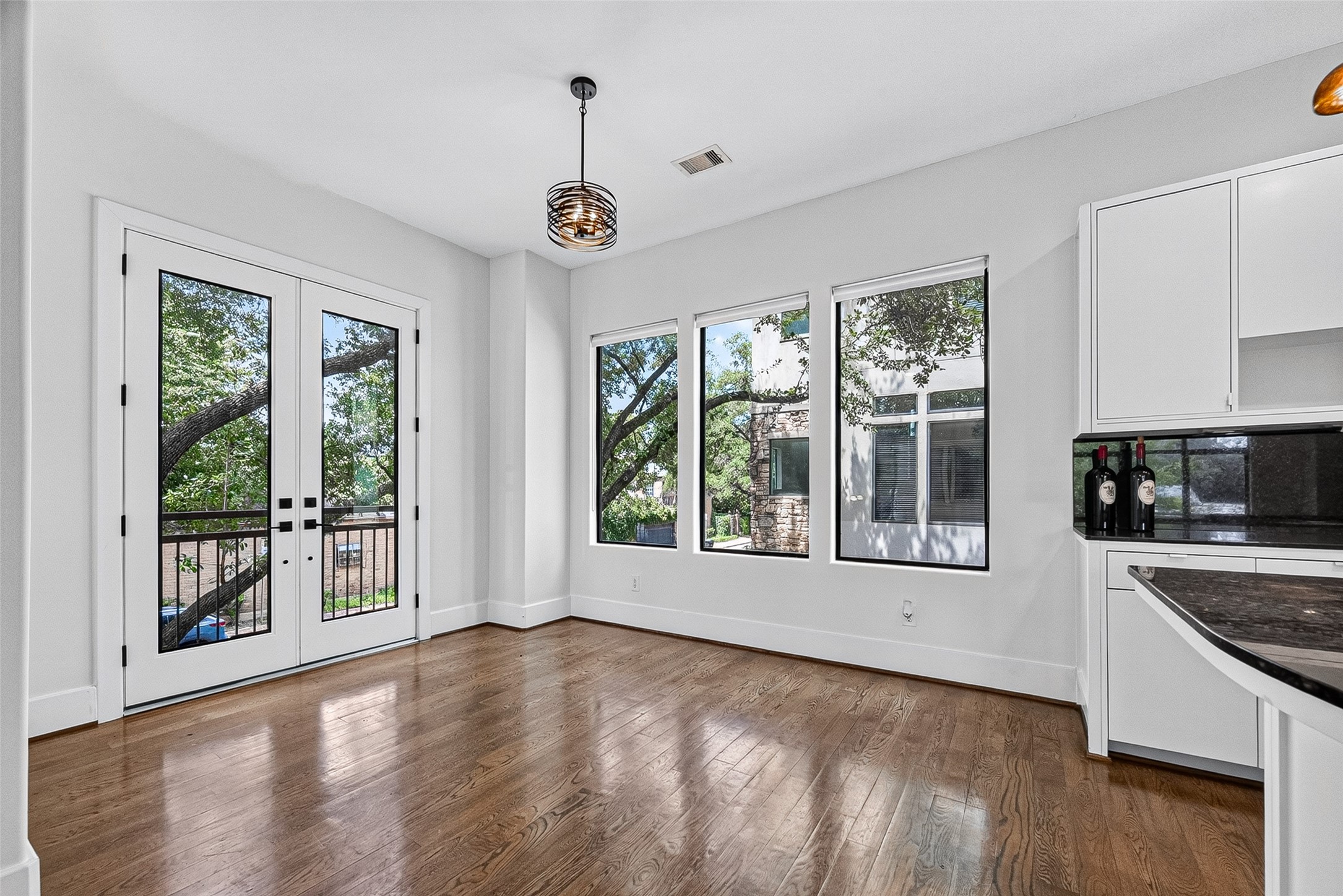 Bright breakfast area with elegant hardwood floors, large windows offering scenic views, and stylish French doors leading to a patio.
