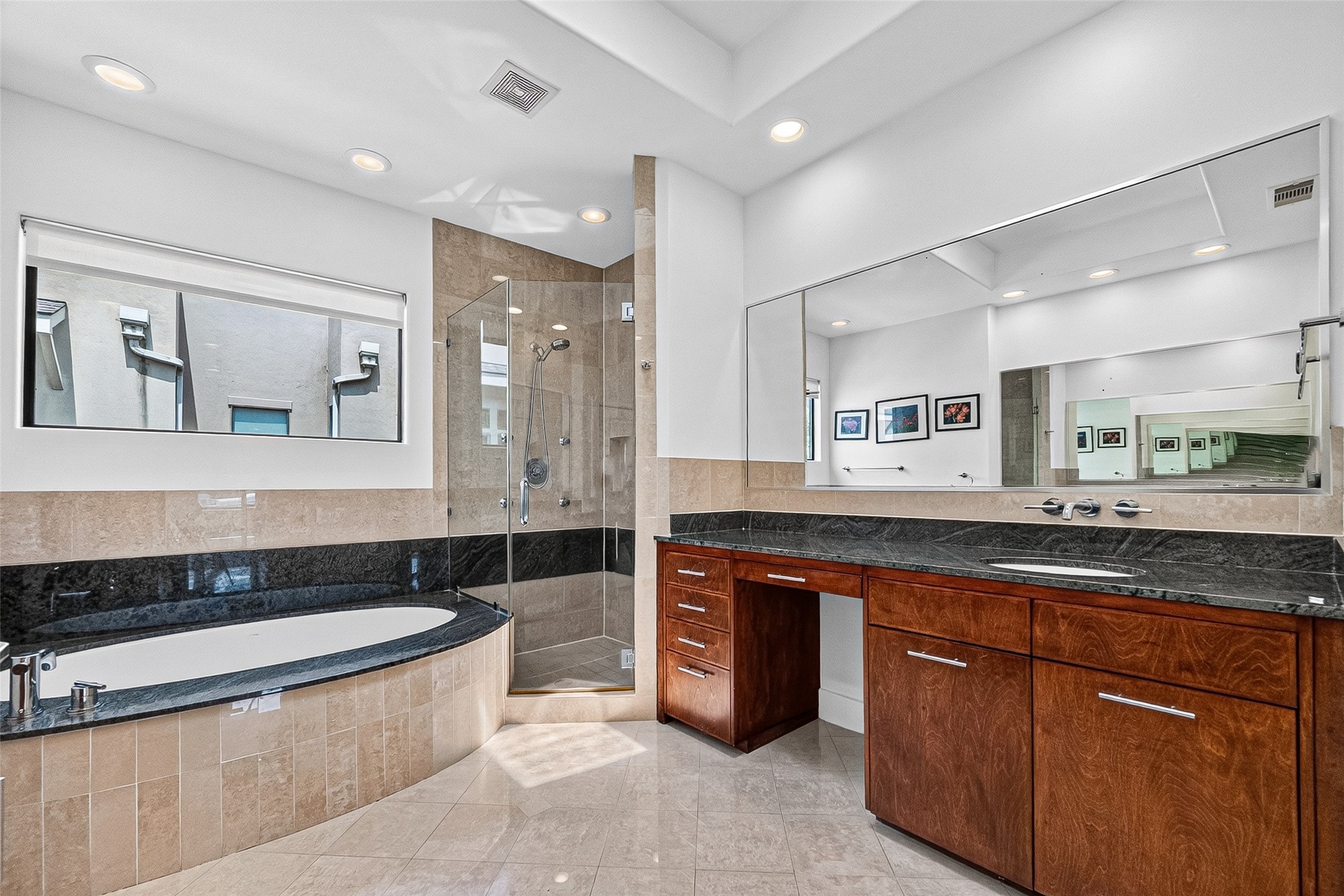 Luxurious primary bathroom featuring a spacious glass-enclosed shower, elegant soaking tub, and sleek vanity with rich wood cabinetry and black granite countertops.