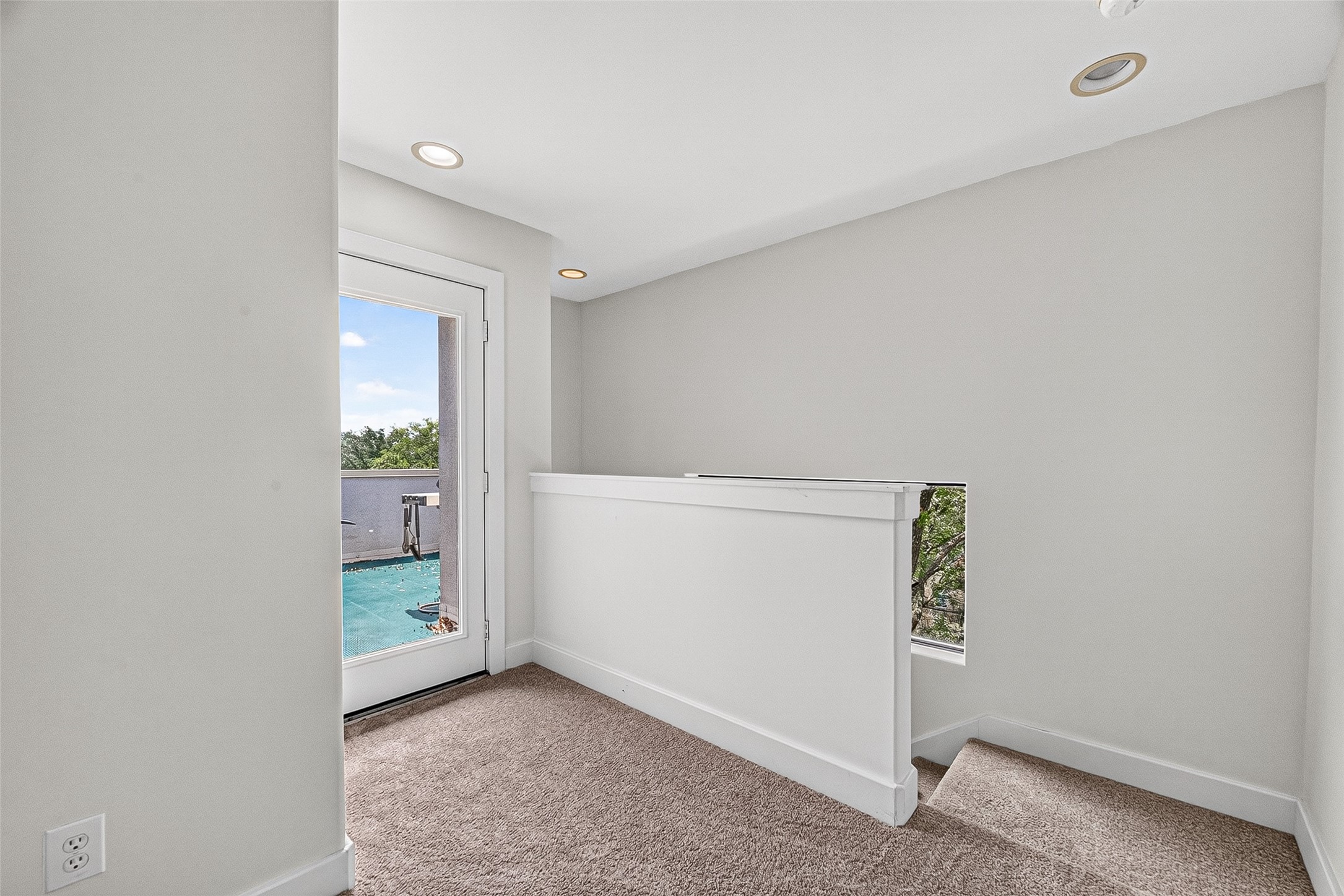 Bright and airy landing area on fourth floor with plush carpeting, recessed lighting, and a door leading to a scenic balcony view.