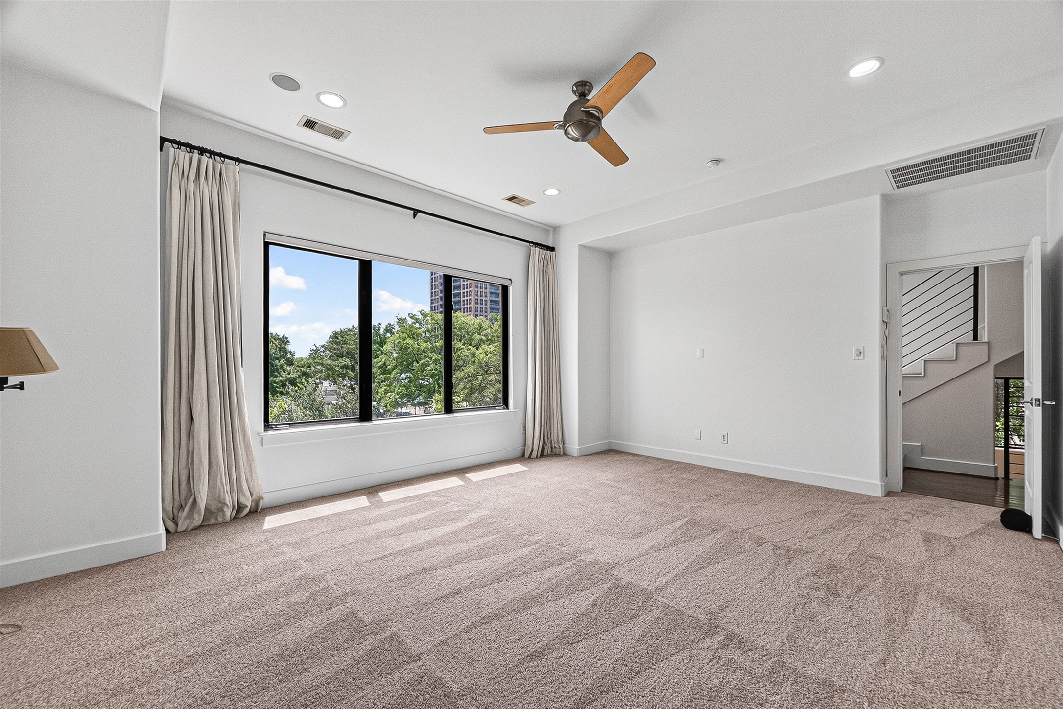 Spacious primary bedroom with plush carpeting, large window offering lush views, and a stylish ceiling fan.