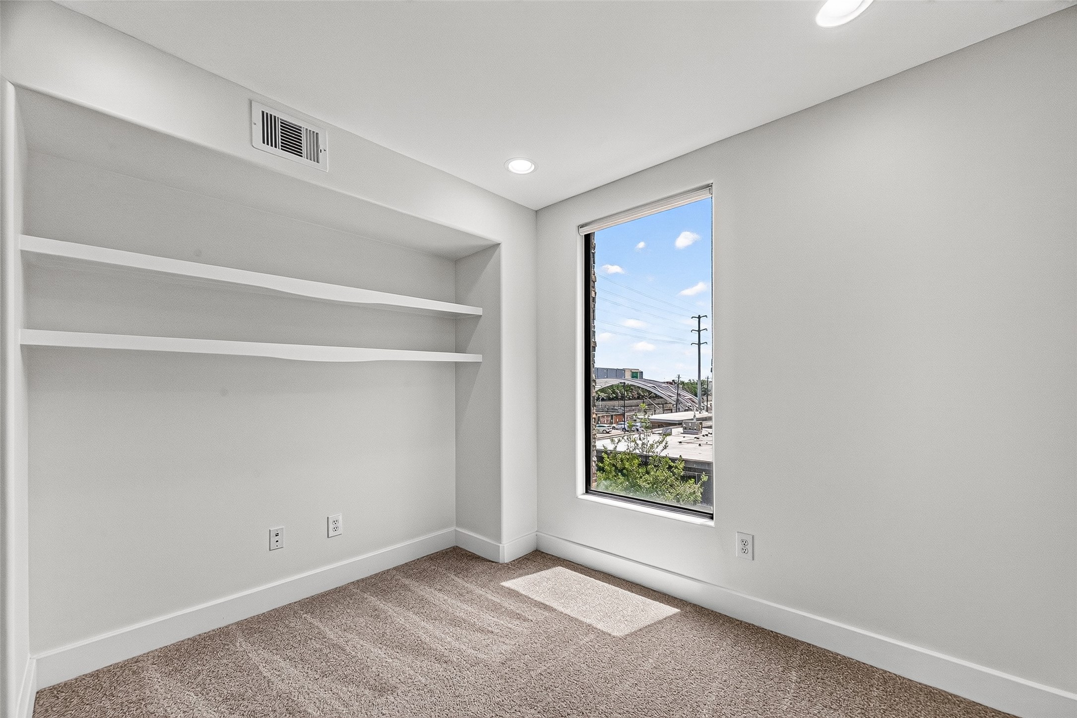 Bright and cozy flex room with built-in shelves, plush carpeting, and large windows offering city views.