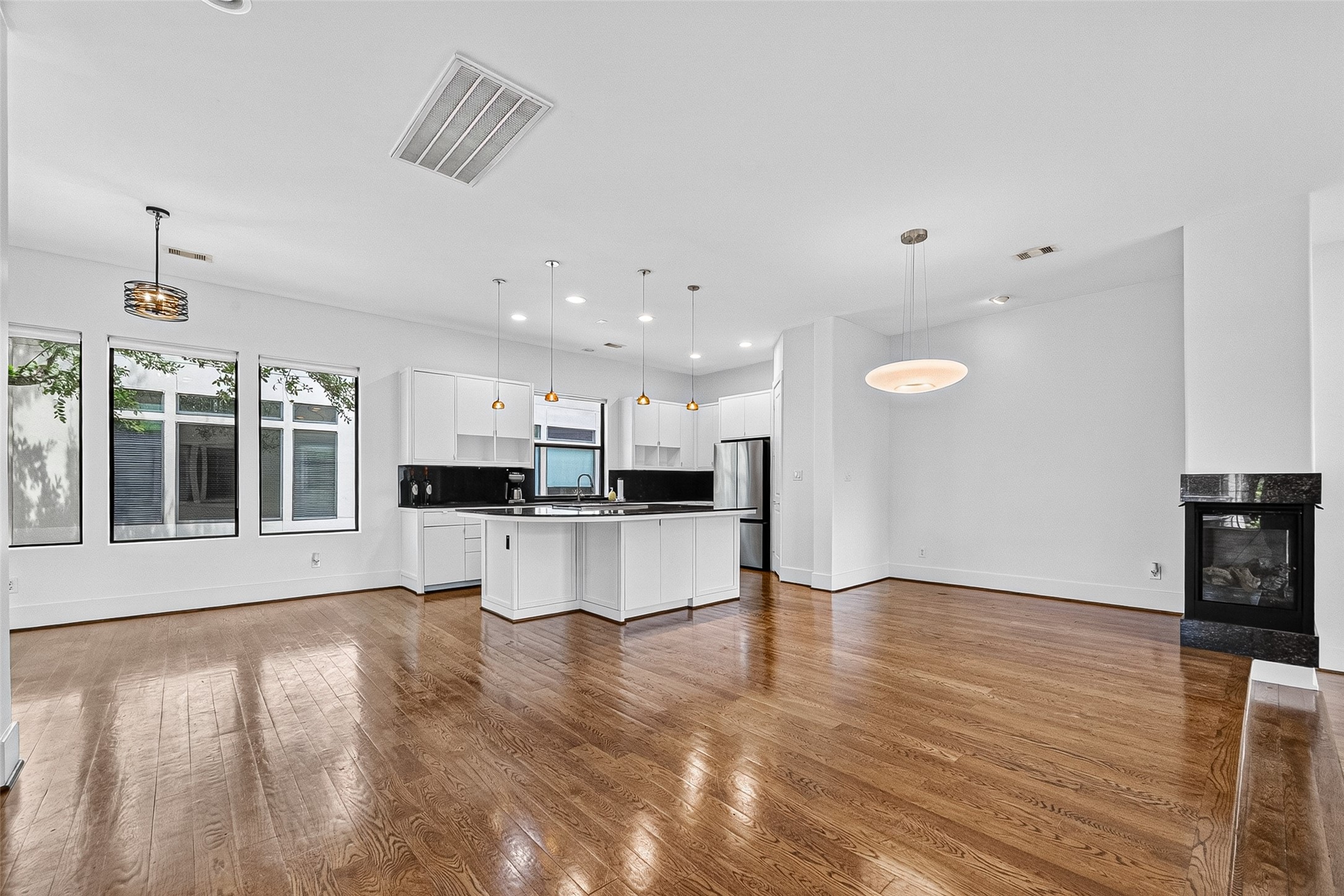 Spacious open-concept living area features sleek hardwood floors, a modern kitchen with a large island, stainless steel appliances, and abundant natural light from large windows.
