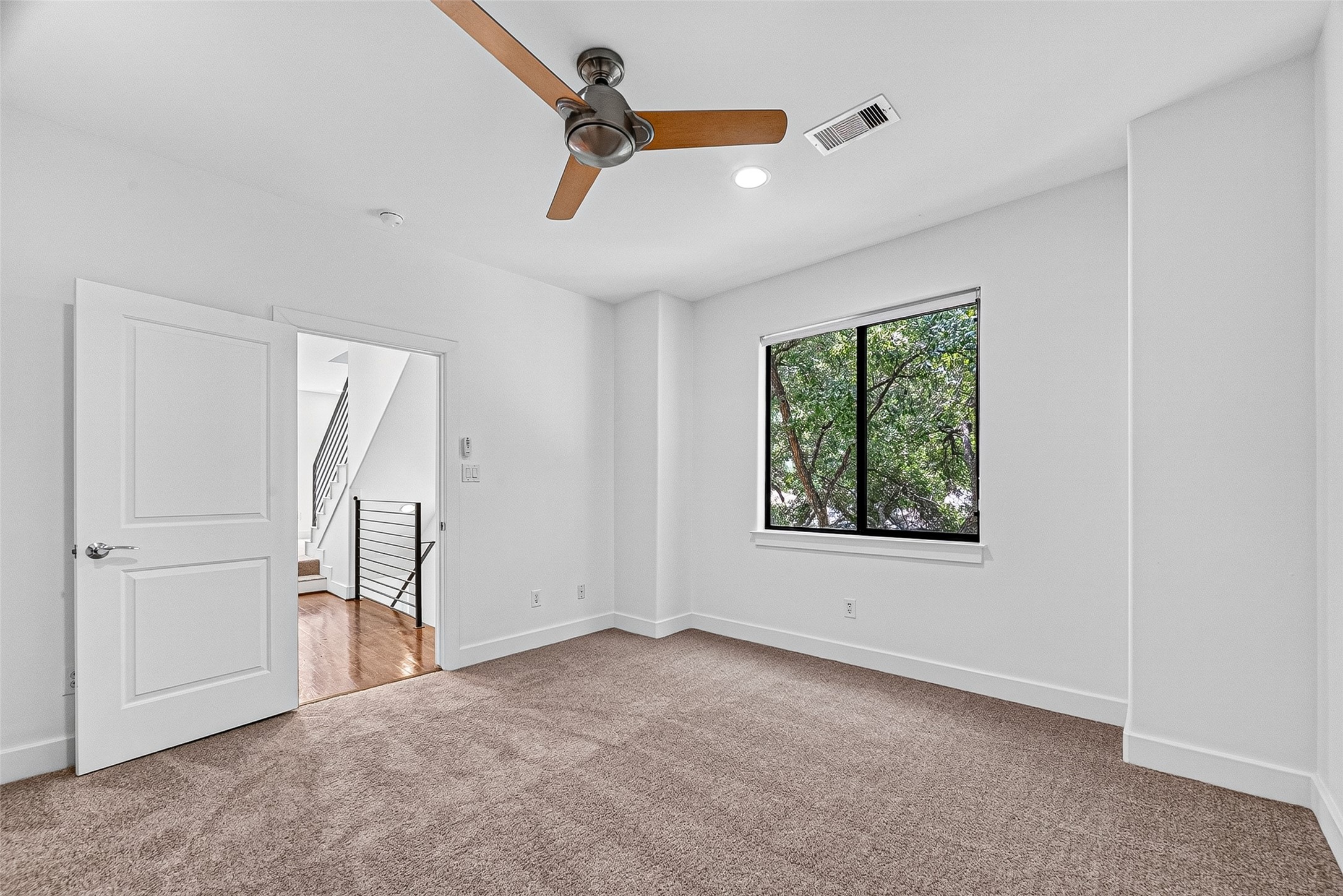 Spacious bedroom on third floor with plush carpeting, features a large window offering views of lush greenery and ample natural light.
