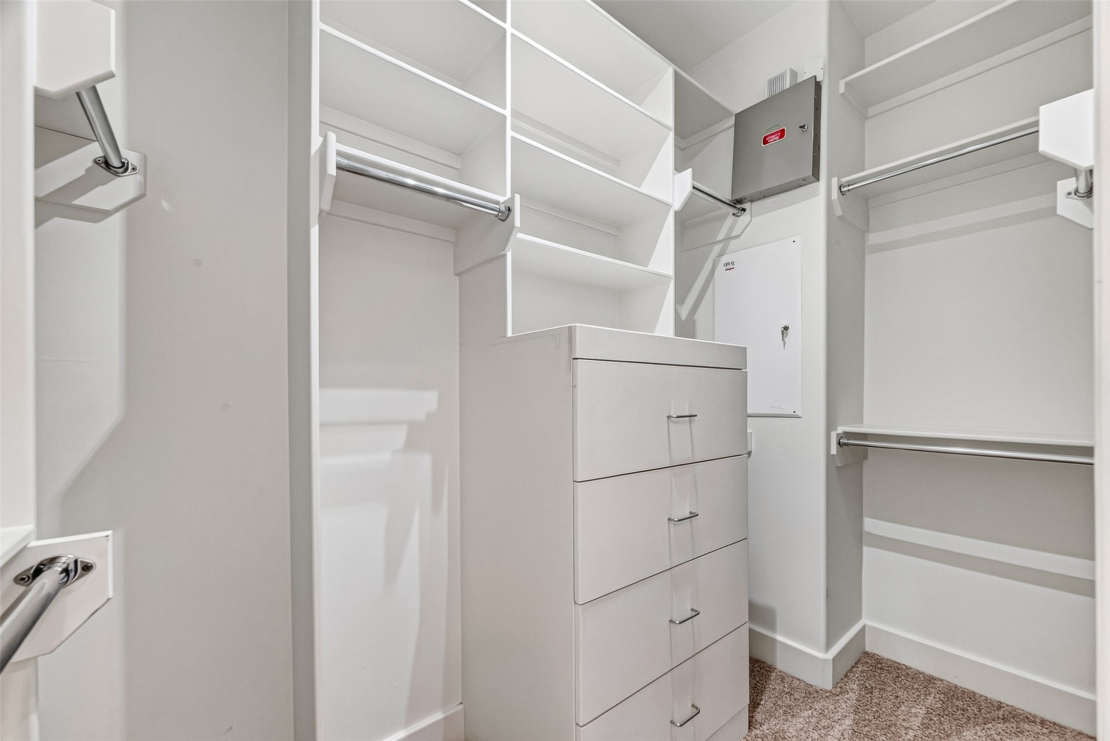 One of two spacious primary walk-in closet featuring ample shelving, hanging rods, and a built-in drawer unit for organized storage.