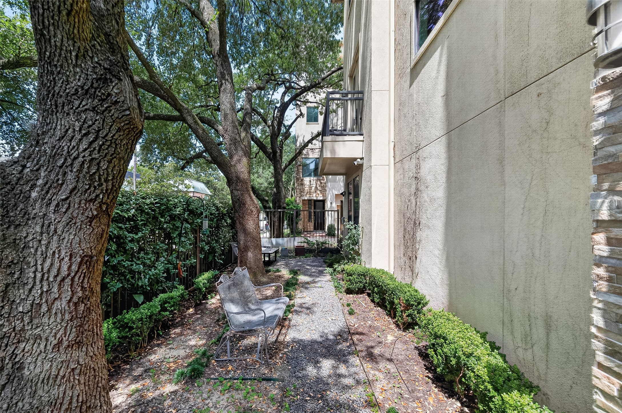 Charming outdoor space with mature trees providing shade, a cozy seating area, and a pathway lined with lush greenery, perfect for relaxation and privacy.
