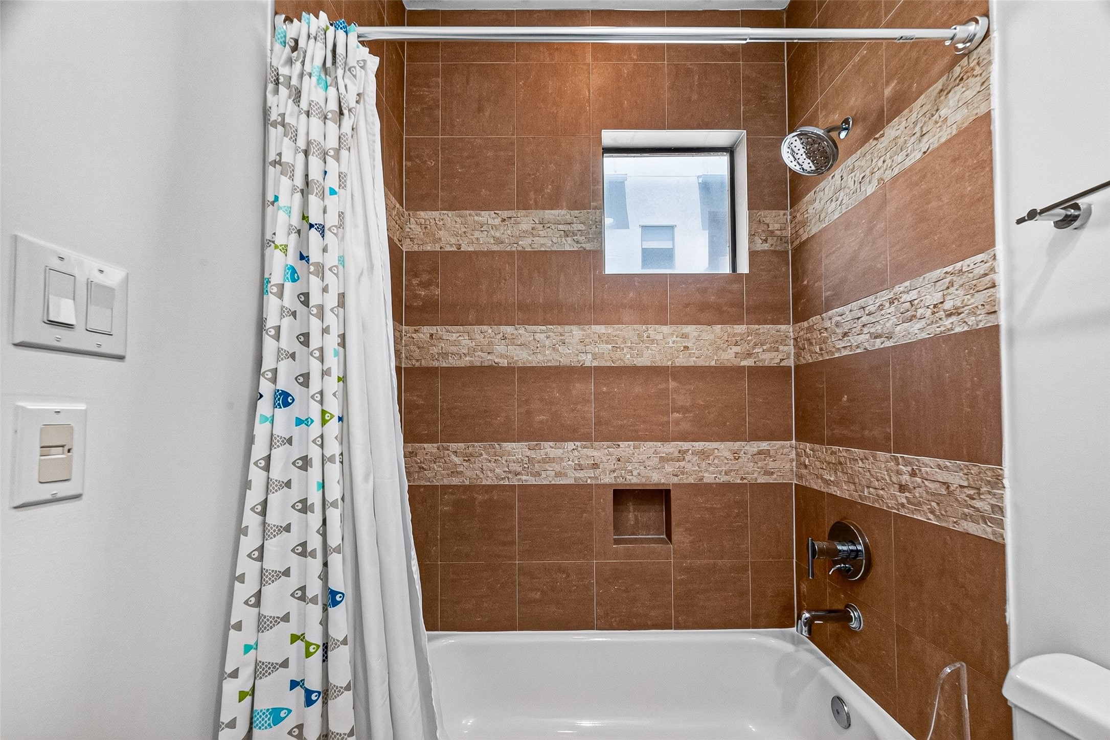 Charming bathroom in bedroom on third floor with elegant brown tilework featuring decorative stone accents, and a modern showerhead.