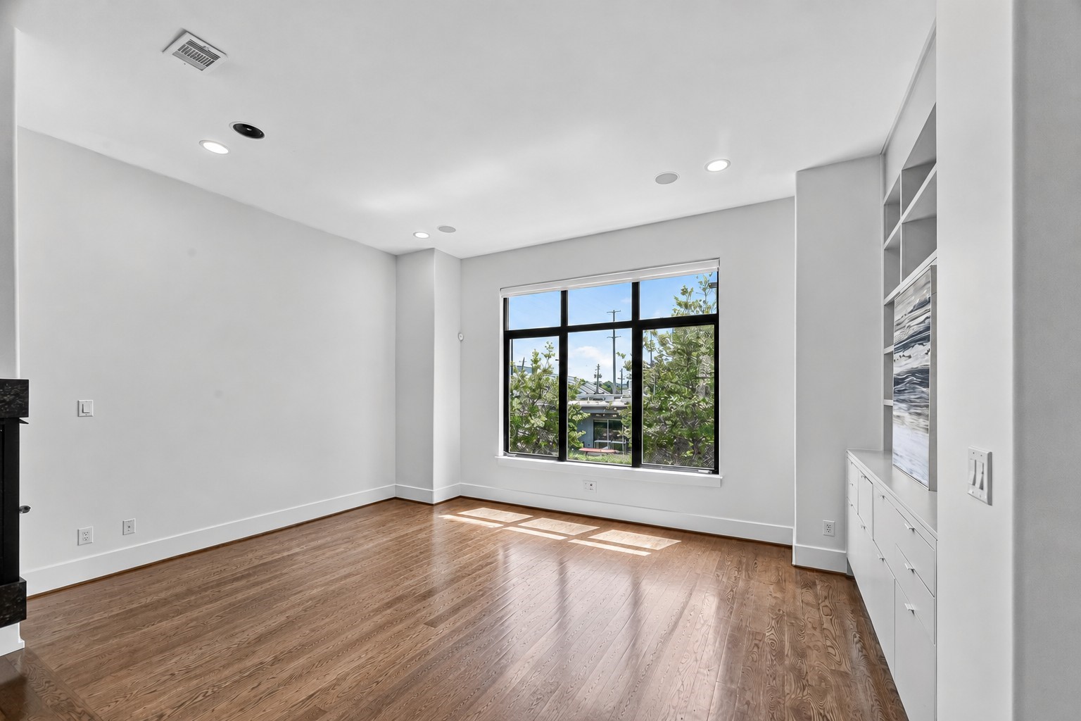 Bright and spacious living room with large windows, sleek built-in shelving, and elegant hardwood floors.