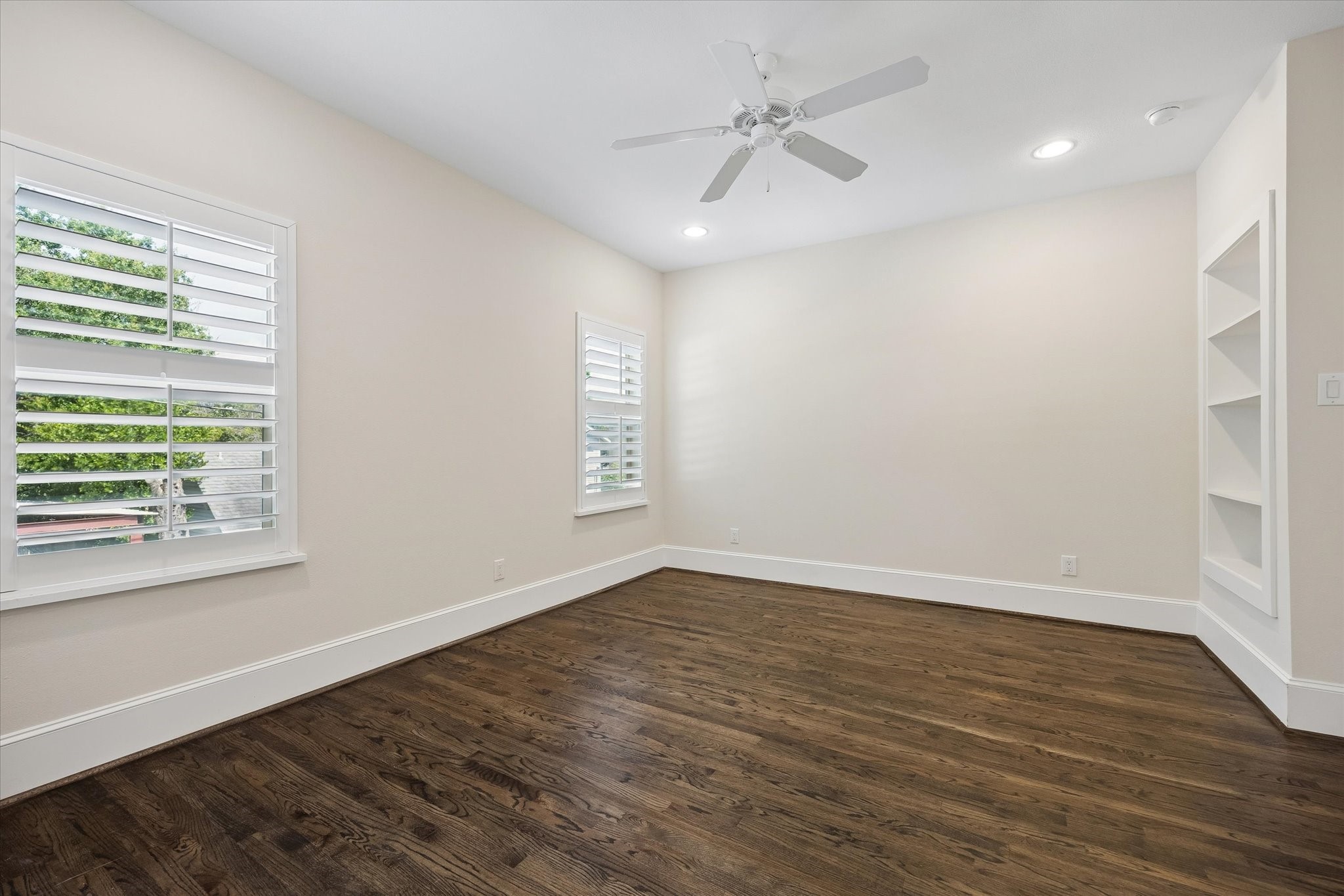 Secondary bedroom with hardwood floors, built-in shelves, ceiling fan, wood shutters, closet and access to a full bathroom.