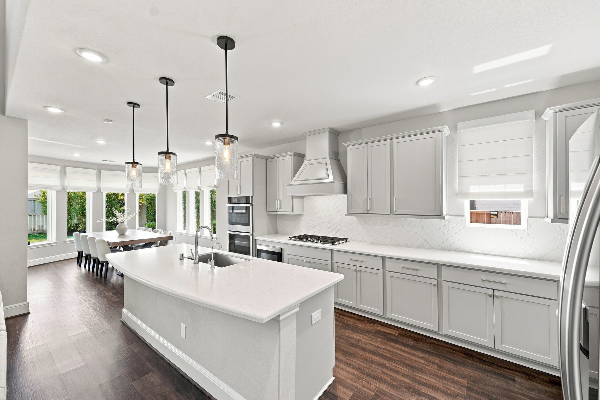 The open-concept kitchen features quartz countertops, oversized island, double ovens, microwave drawer and remote Roman shades. The open-concept kitchen features quartz countertops, oversized island, double ovens, microwave drawer and remote Roman shades.