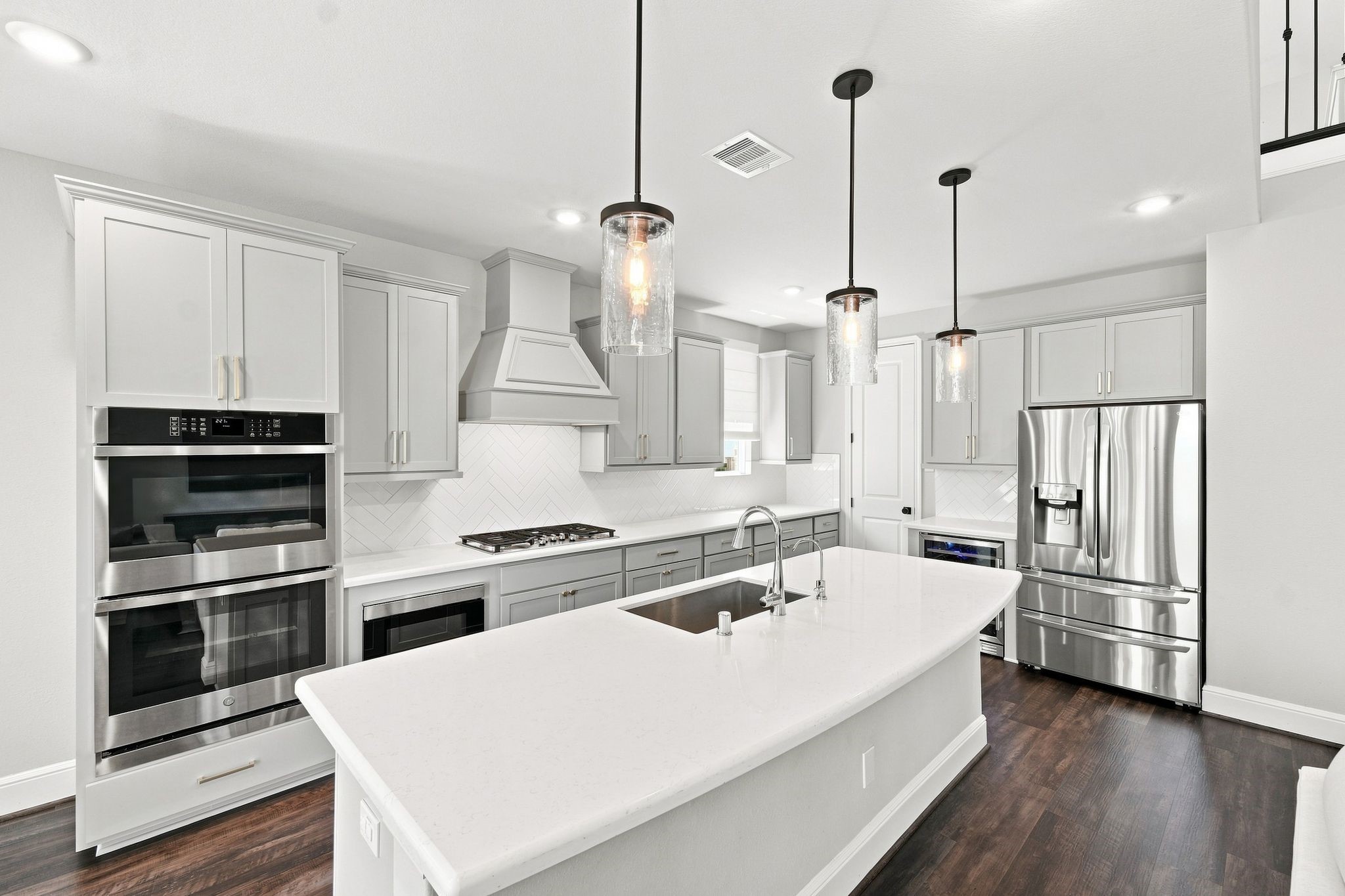 The open-concept kitchen features quartz countertops, oversized island, double ovens, microwave drawer and remote Roman shades. Walk in pantry is accessible through the door in the corner.
