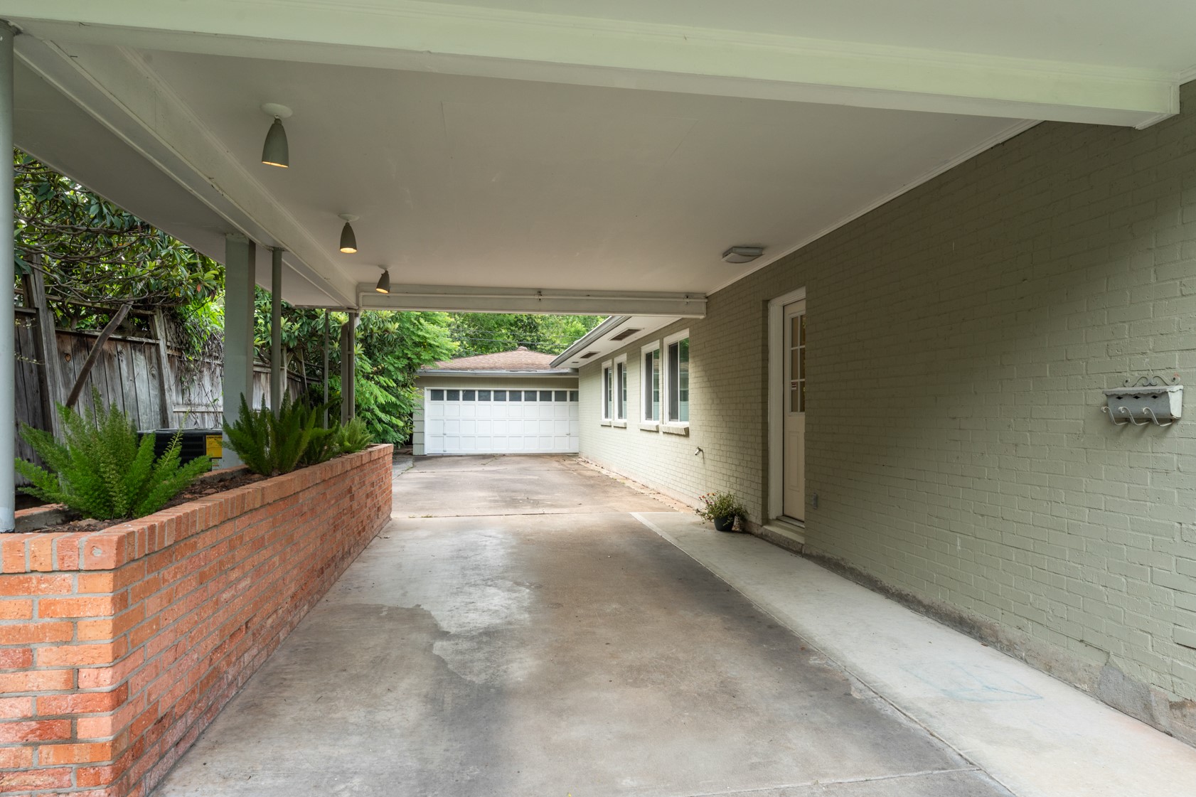 A PORTE-COCHERE keeps you and your car protected from rain and summer sun. Note the original mid-century modern overhead lighting on the left.  Side entry door on the right. The detached 2-car garage is oversized allowing for extra storage space.