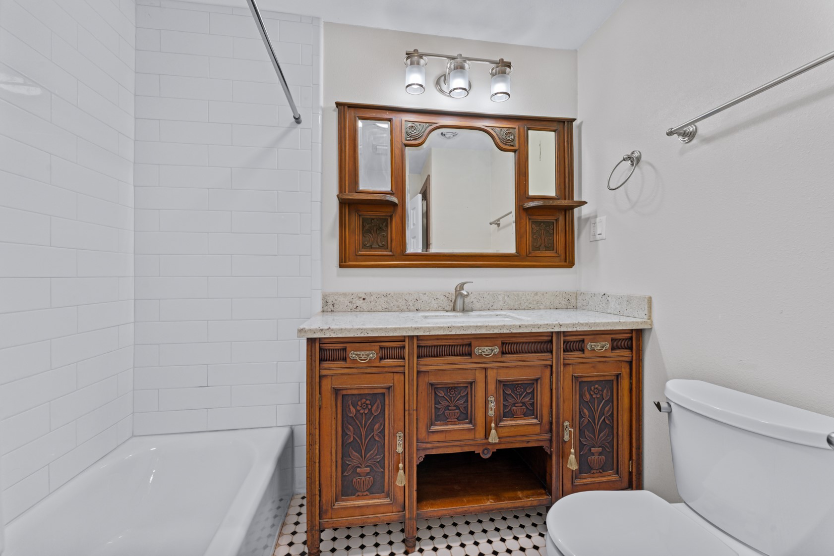The hall bathroom mixes carefully restored antique pieces with modern finishes - tub and shower, white subway tile, granite counter, beautiful vanity and mirror, and vintage-style black and white tiled floor.