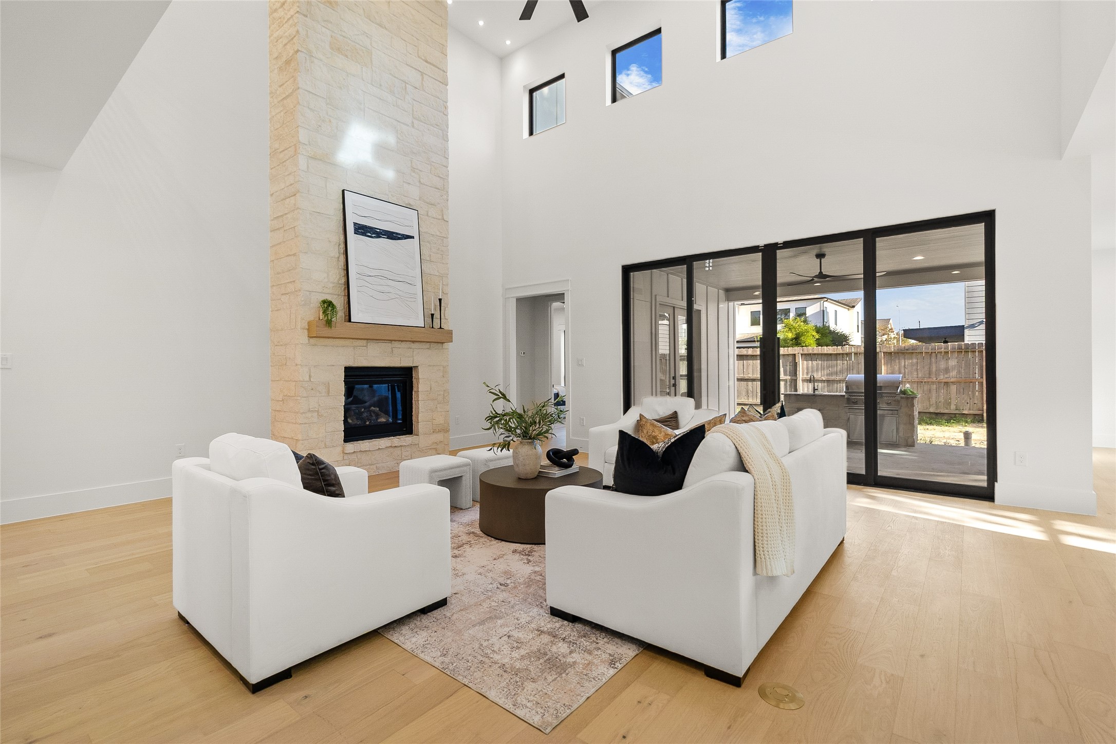 A floor-to-ceiling stone fireplace anchors this two-story living room, topped with a wood mantel and framed by stacked stone. Soaring ceilings and a row of clerestory windows bring in natural light, while sliding glass doors open to a covered outdoor living area with a built-in kitchen. Wide-plank hardwood floors and an open layout make this a comfortable space for gathering and relaxing. A floor-to-ceiling stone fireplace anchors this two-story living room, topped with a wood mantel and framed by stacked stone. Soaring ceilings and a row of clerestory windows bring in natural light, while sliding glass doors open to a covered outdoor living area with a built-in kitchen. Wide-plank hardwood floors and an open layout make this a comfortable space for gathering and relaxing.