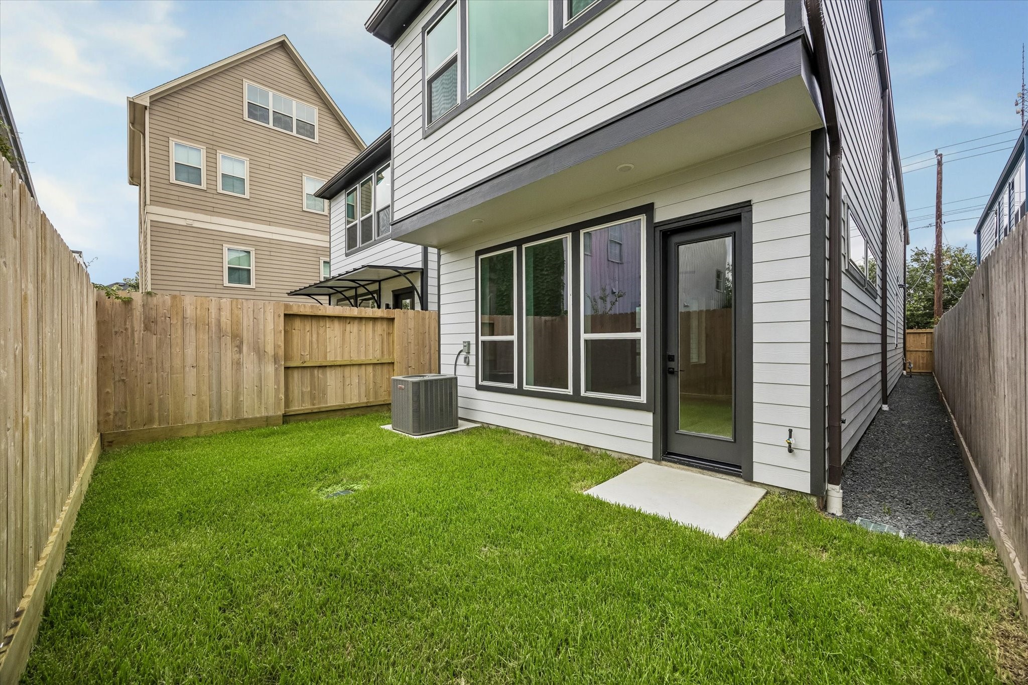 Charming backyard featuring a well-maintained lawn, private fencing, and a modern exterior with large windows and a sleek back door for easy outdoor access.