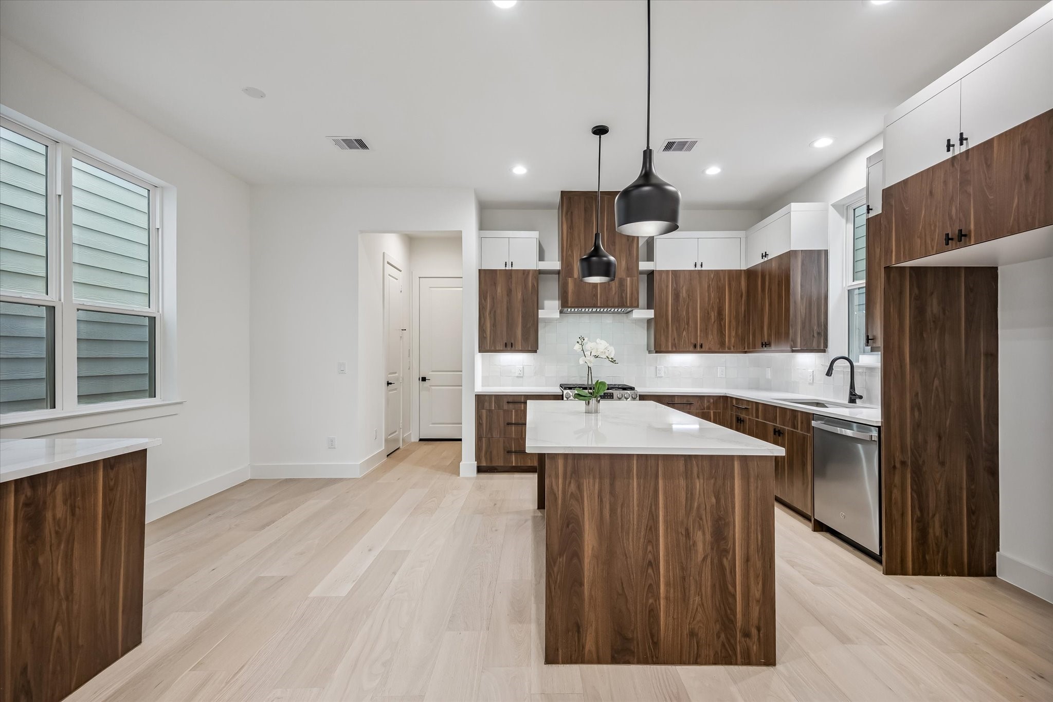 Discover a modern kitchen with sleek wood cabinetry, a spacious island, and stylish pendant lighting, complemented by stainless steel appliances and ample natural light.