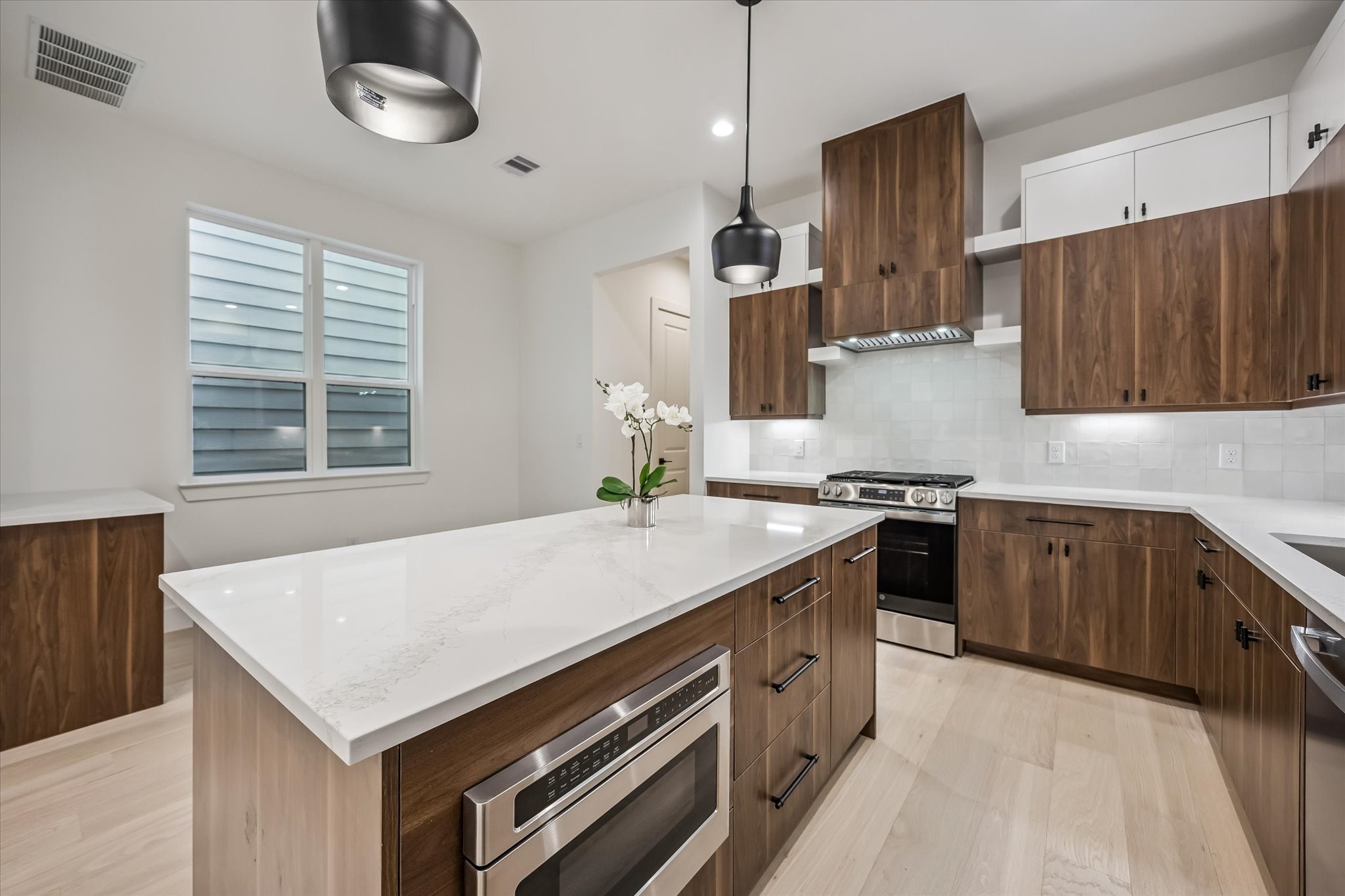Stunning modern kitchen with sleek wood cabinetry, a spacious island with a built-in microwave, and elegant pendant lighting, creating a perfect blend of style and functionality.