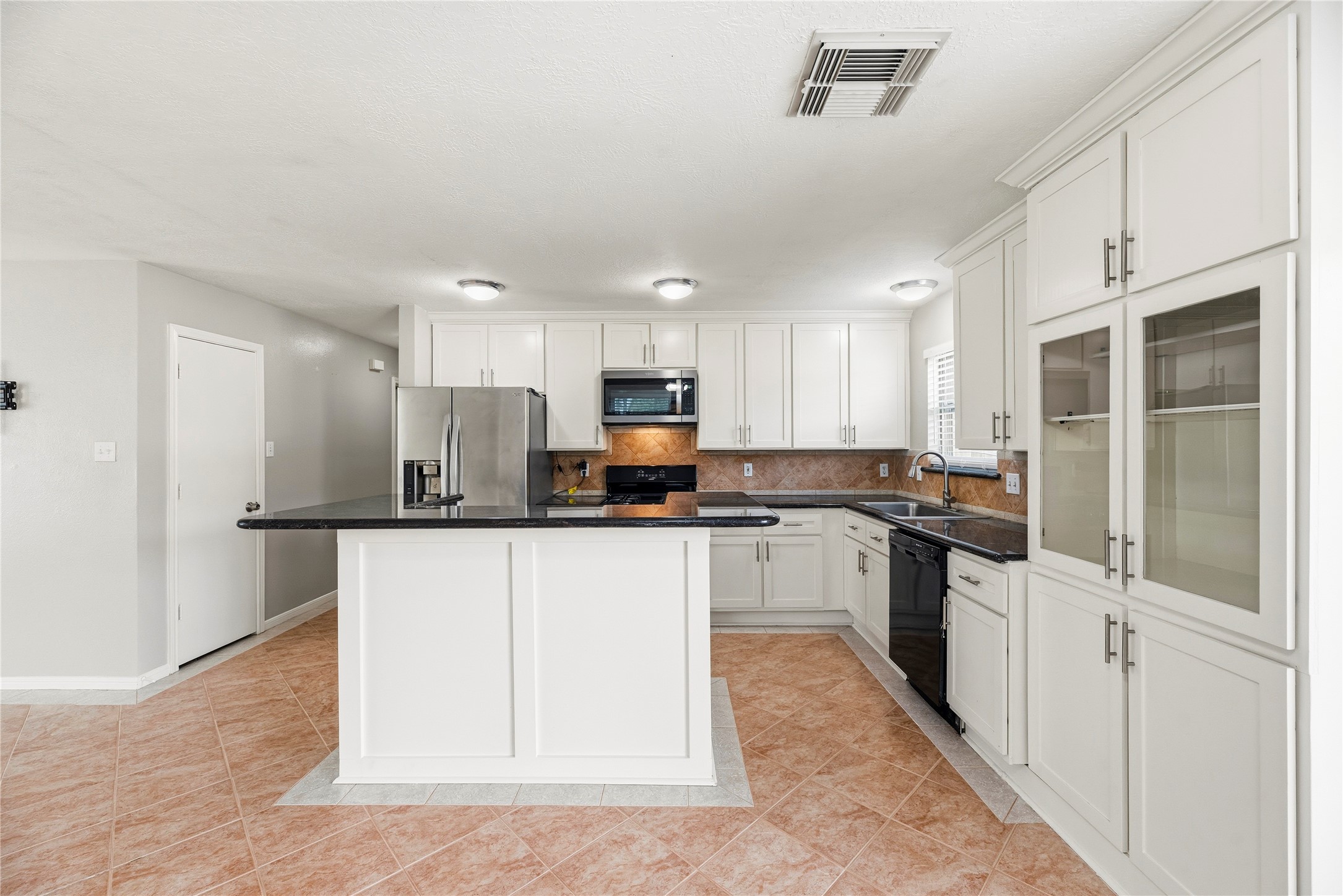 The kitchen offers white cabinetry, tile backsplash, granite countertops and a gas range.
